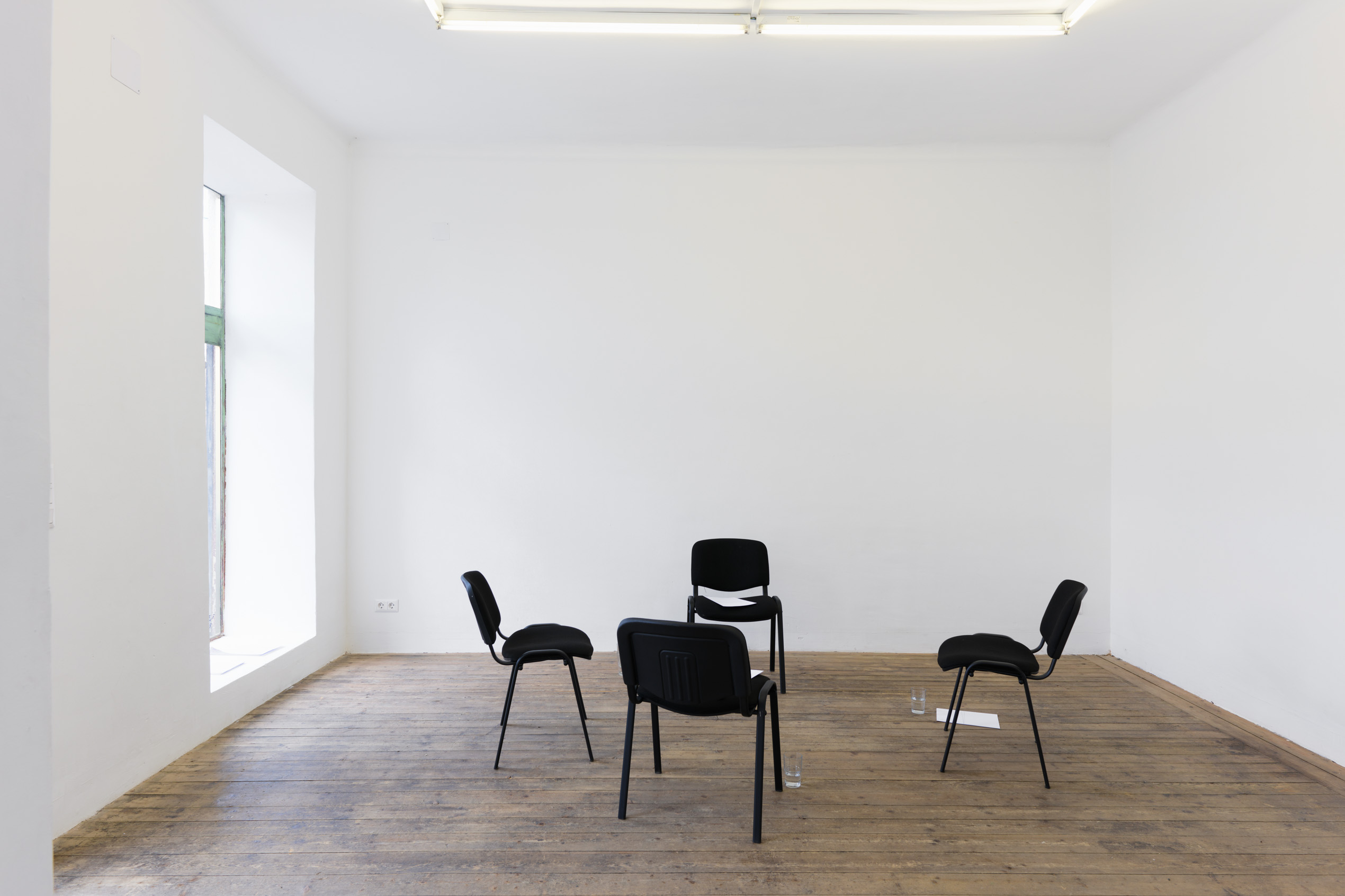 Aaron Amar Bhamra: “a choir of four voices”, 2024. Variable Dimensionen. Bedrucktes Papier, Bleistift (1. Sopran, 2. Sopran, 1. Alt, 2. Alt), vier Stühle, Gläser, Wasser. Foto: Maximilian Anelli-Monti.