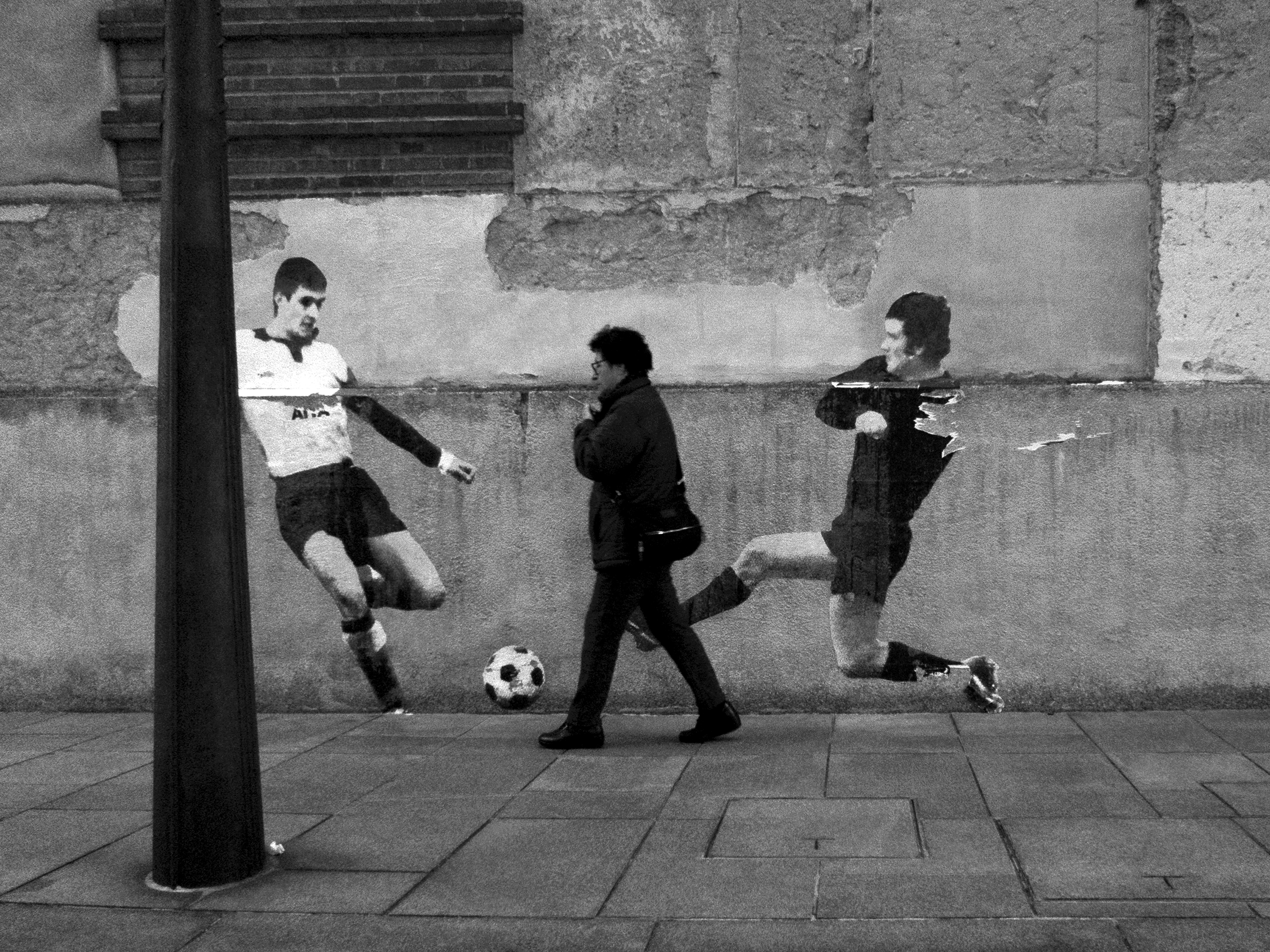 Woman passing by soccer graffiti Pamplona, Spain, 2022photography, bw, single