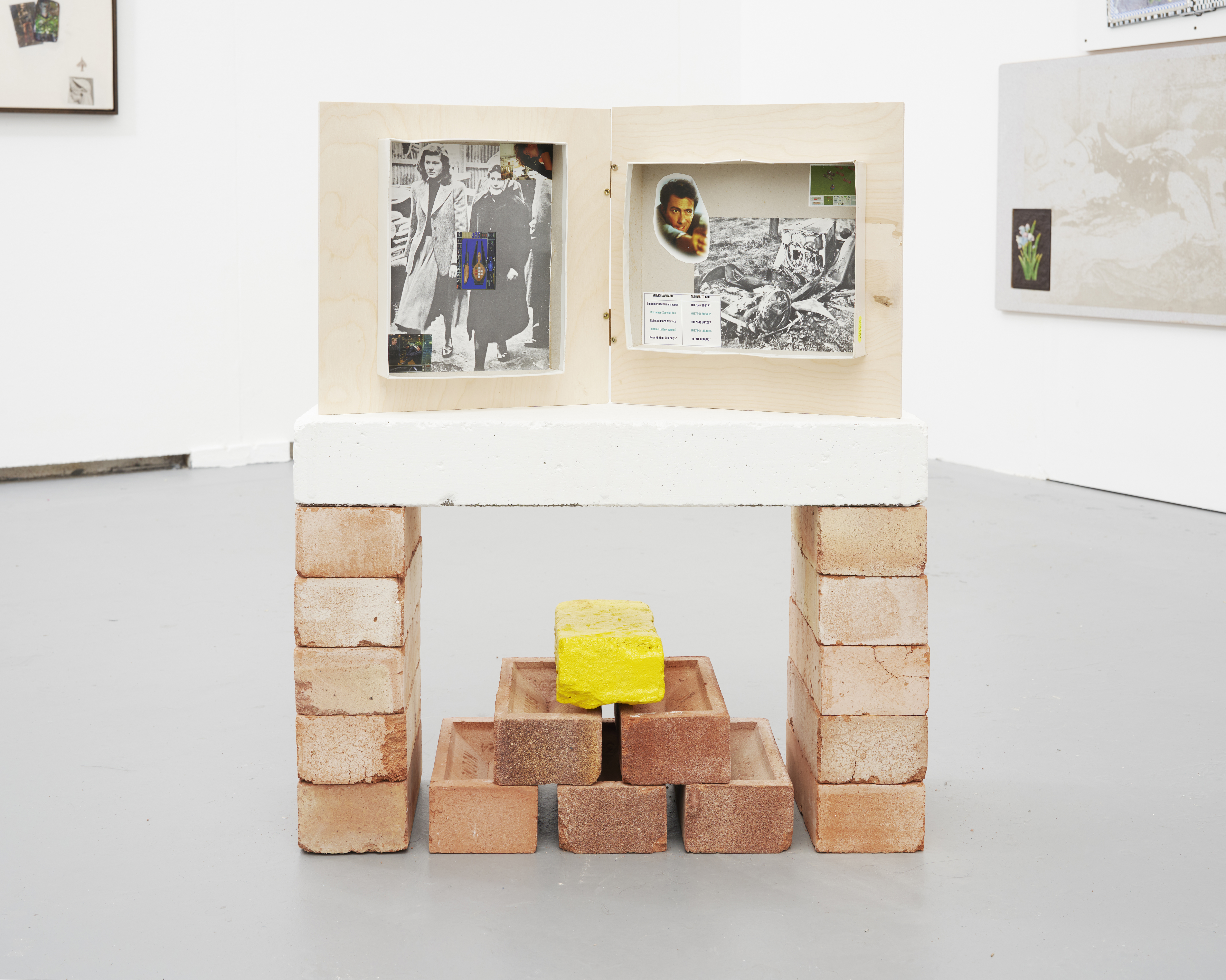 PVP (Player vs Player), 2022, Photo-cut-outs in cardboard video-game boxes, mounted to ply W/ coloured dice, 31x57x7cm  + Yellow brick from the yellow brick road, 2022, brick and high-visibility road paint, 21x10x7cm