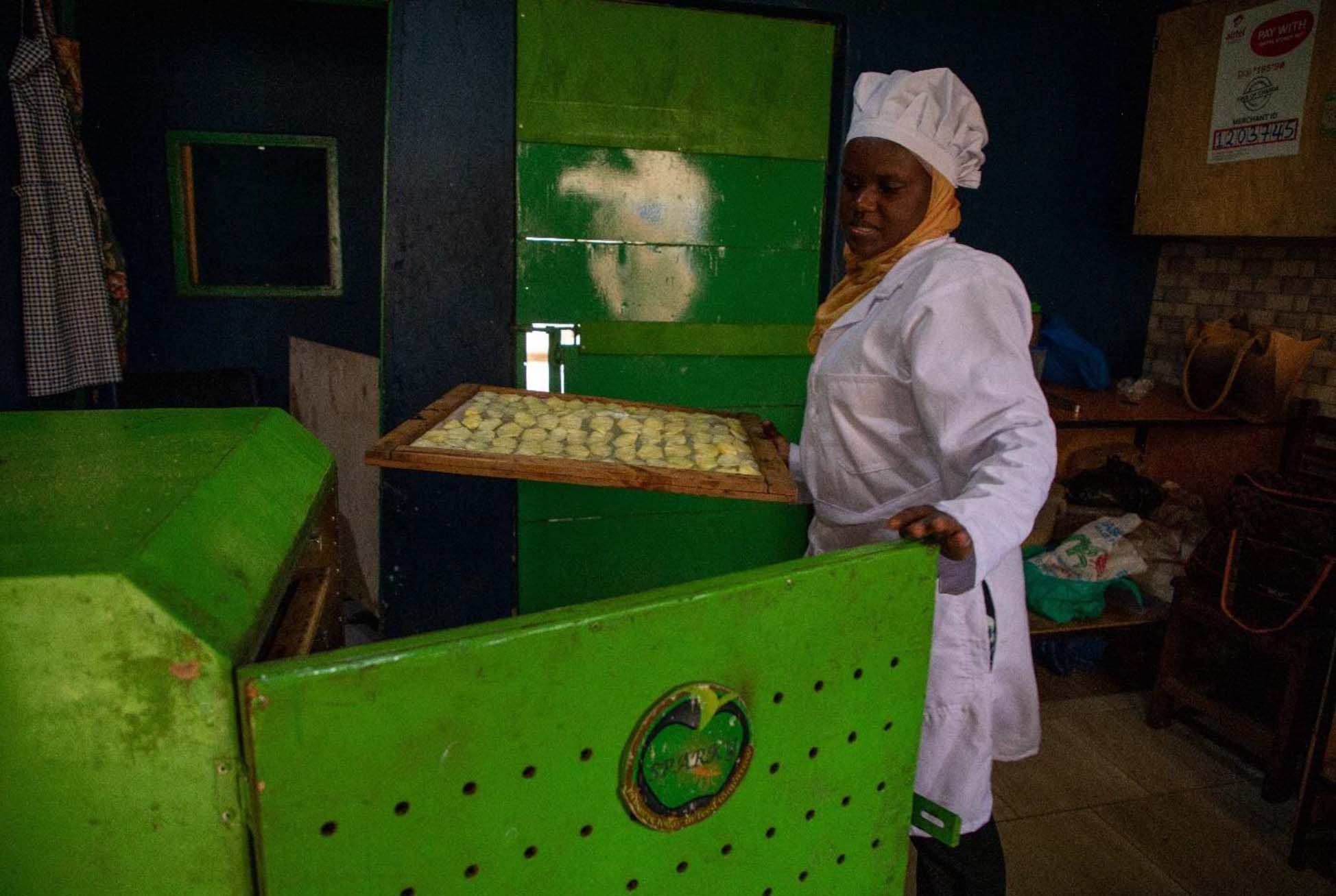 Faridah place le casier d'ananas dans le séchoir Sparky. L'entreprise, basée à Kyebando, fabrique des séchoirs de différentes capacités et de différents types, et propose également des formations en transformation alimentaire.