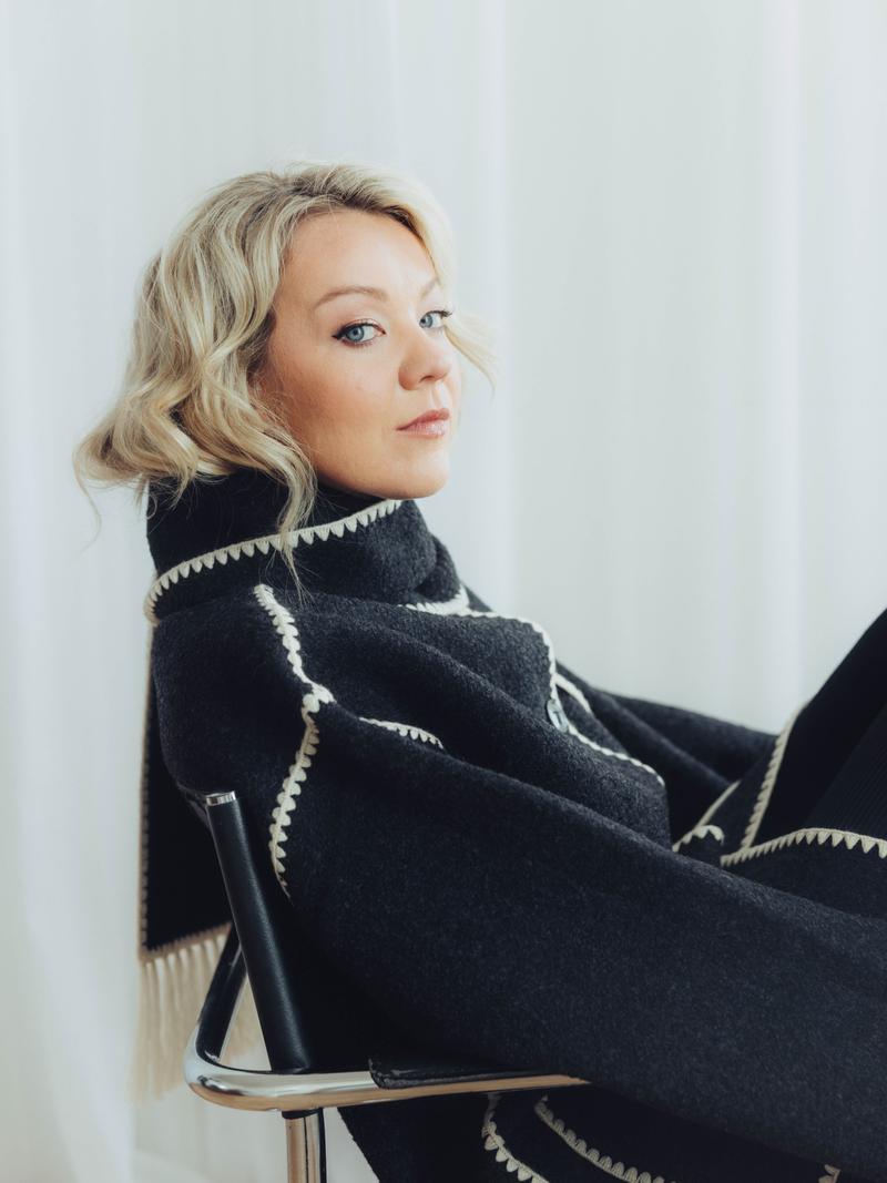 Sarah McBriar, Founder & Creative Director of UP! Productions, seated in a dark coat with white detailing.