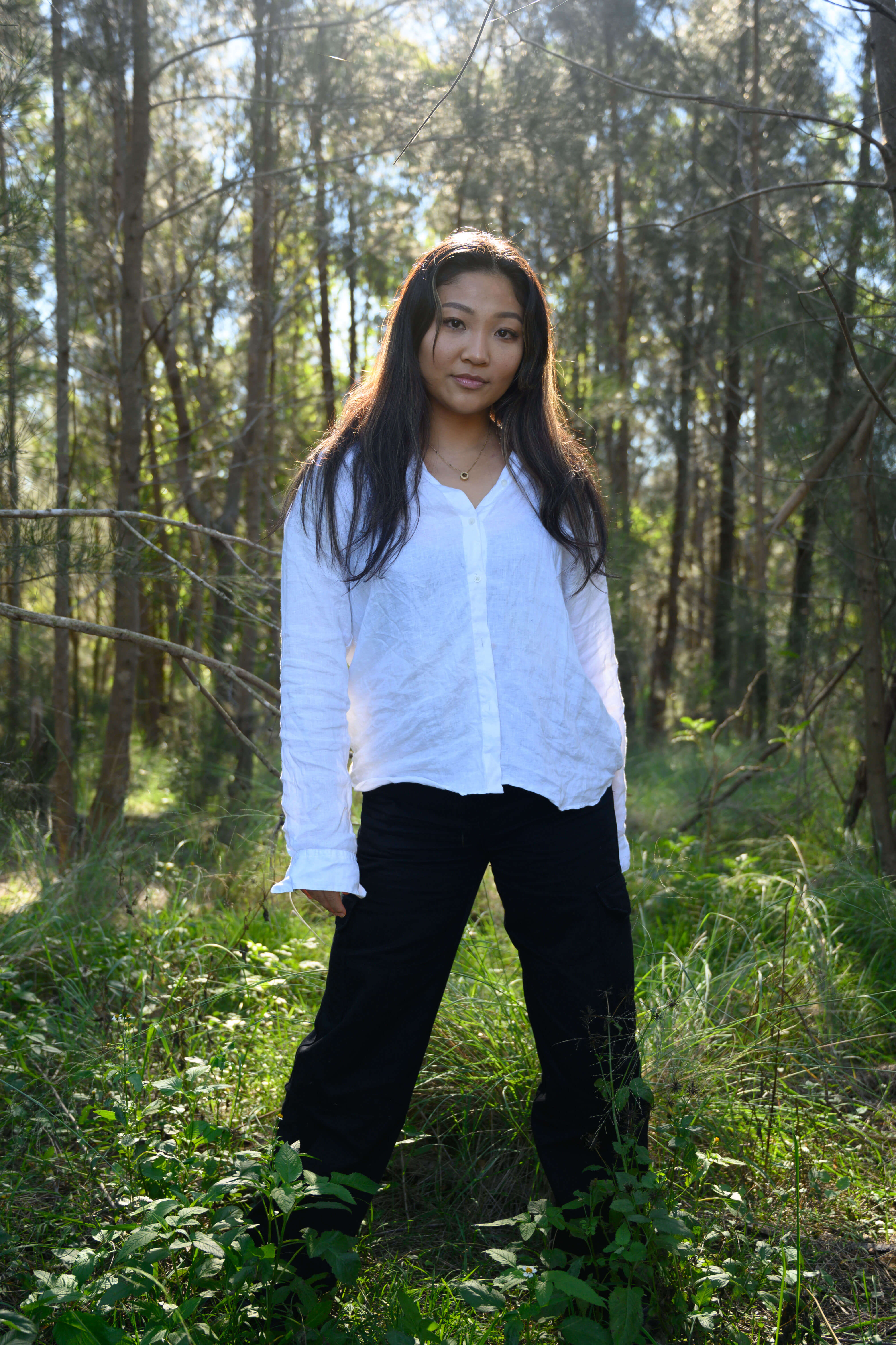 Kim stands in the middle of some grass. Light shines from above and behind her, creating a halo effect behind her head.
