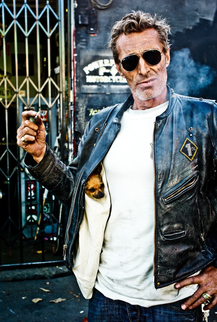 Portrait von Rudy Verwey mit Hund Tiffany. Im Hintergrund sieht man das Eisengitter zur Werkstatt.