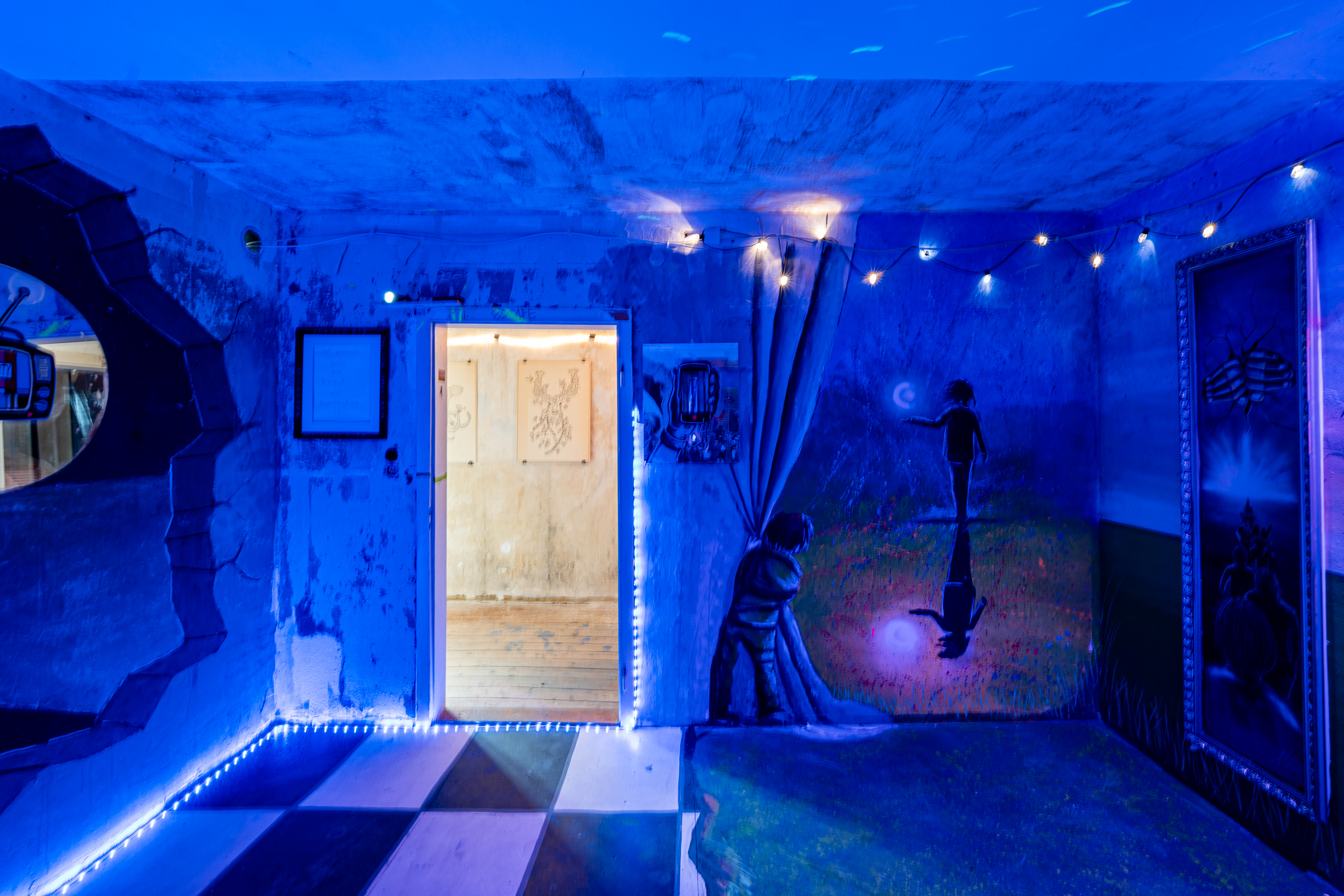 Bild 2 Eyes Wide Shut: Blick im Raum auf Eingangst&uuml;r. Auf der Wand neben der Eingangst&uuml;r befindet sich eine Wandmalerei, die ein Kind zeigt, das einen Vorhang zur Seite schiebt. Dadurch ist der Umriss einer Person erkennbar, dessen Schatten sich im Mondlicht spiegelt.