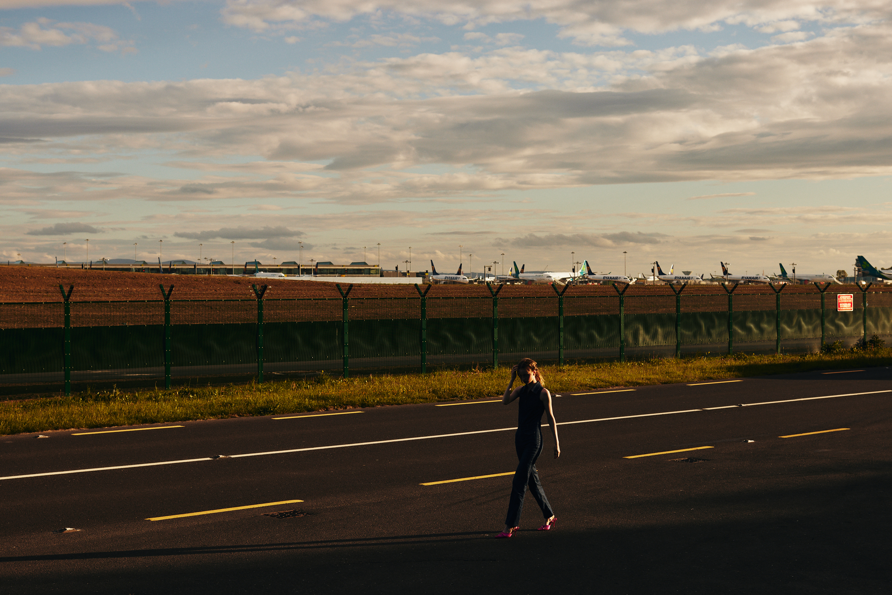 Stylish fashion editorial photoshoot in Dublin, Ireland, featuring a beautiful model in vintage clothes. Captured by a talented photographer for Totally Dublin magazine, this photography showcases the city's unique fashion scene and the beauty of vintage clothing with airplanes in the background. Fashion shoot at an airport.