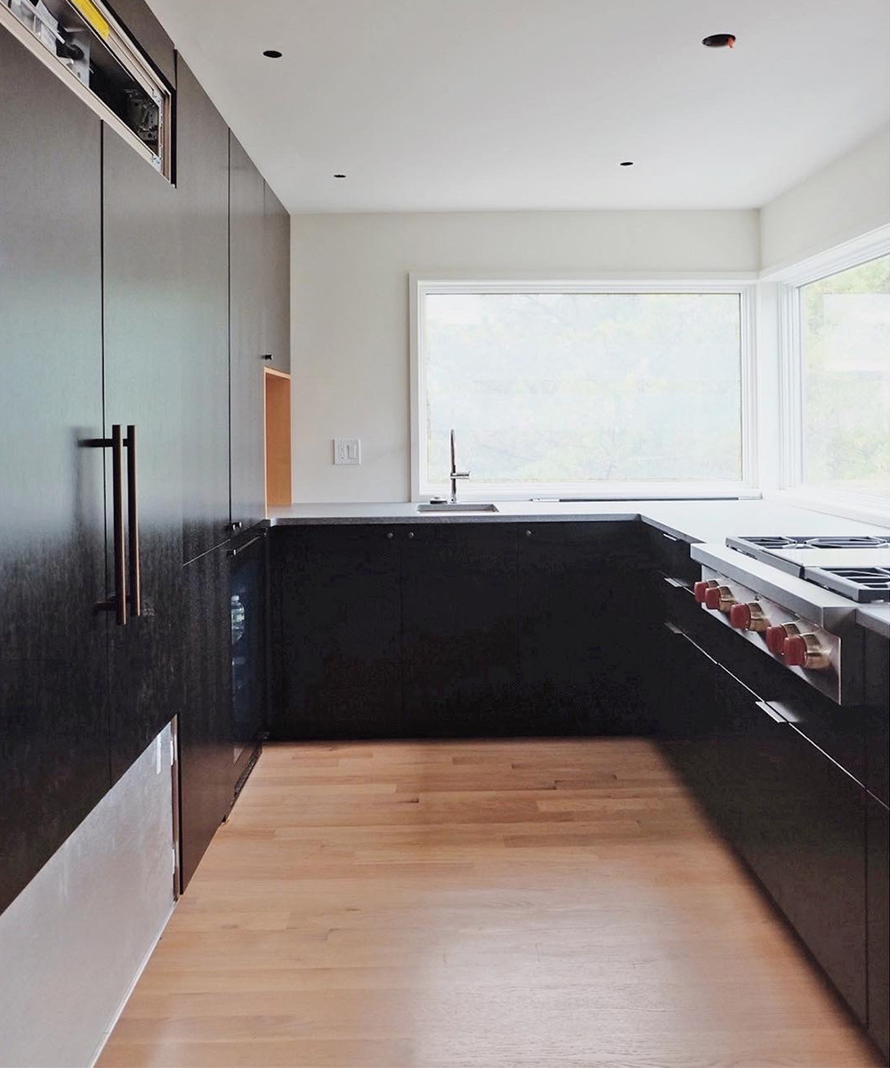 Interior photo of the Brant Beach renovation kitchen, featuring a long counter space with a large window and modern black base cabinetry with light wood floors.