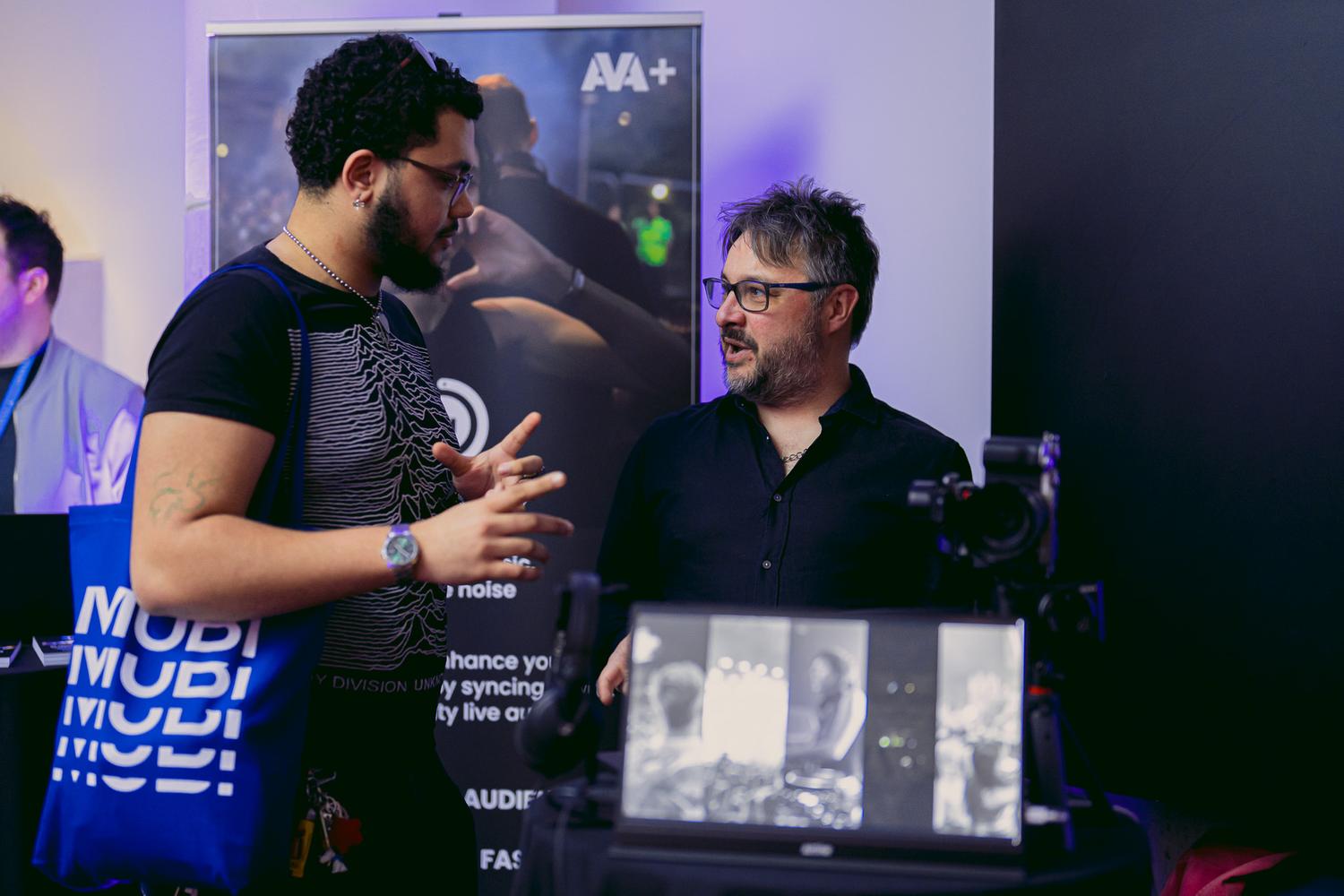 Attendees engaging in conversation at AVA London 2025 with AVA+ branding visible in the background.