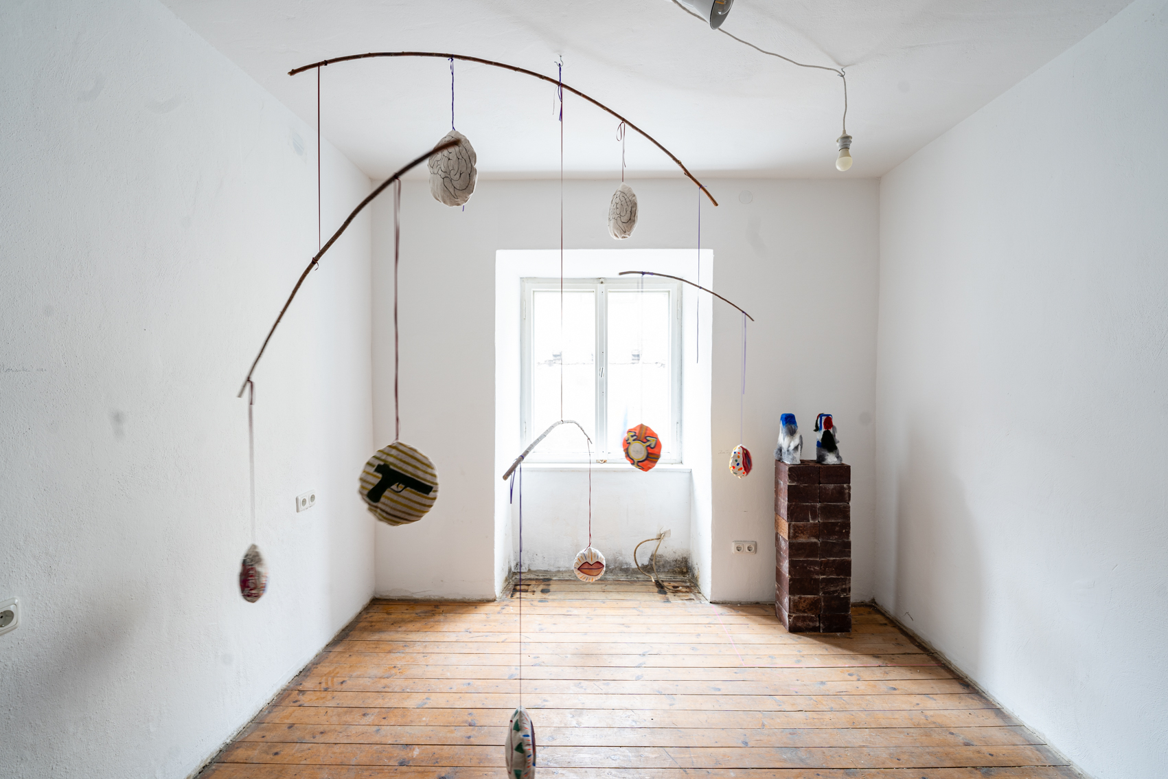 Bild 3 zu Un&ne;gleich: Ein Mobile h&auml;ngt im Raum. Leicht gebogene &Auml;ste, daran h&auml;ngen Runde zusammengen&auml;hte Stoffkreise, mit verschiedenen Motiven darauf.