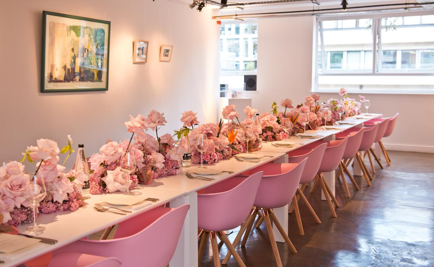 Long dining table at Glossier London event decorated with pink roses and floral centrepieces.