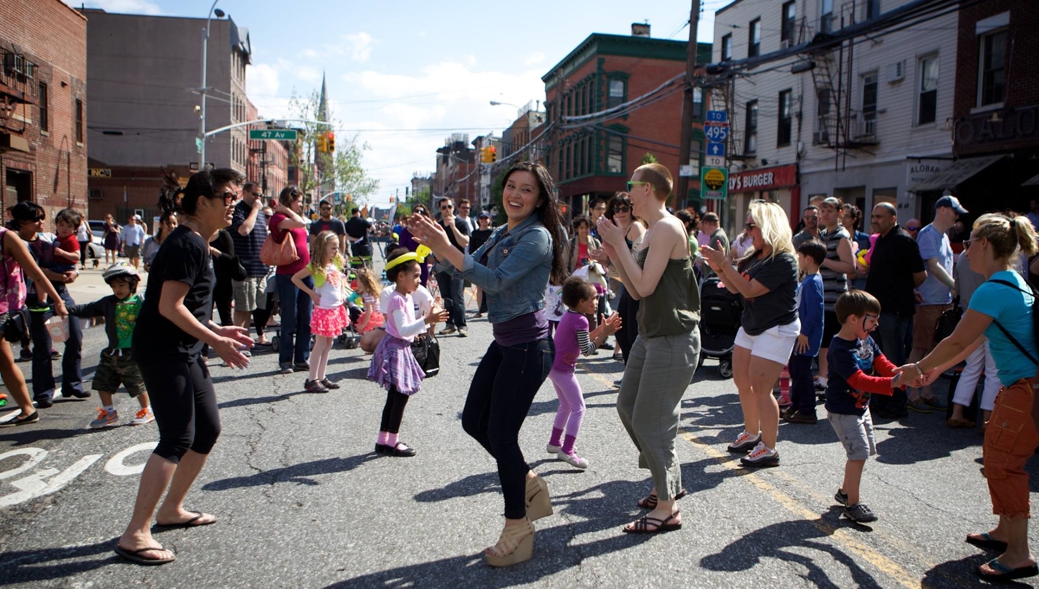 A diverse group of people perform a line dance at an Avenue NYC event in Long Island City, Queens.