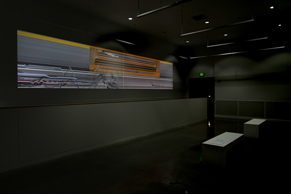 A video projection of abstract lines, patterns, and forms and two benches placed in front of the projection in a dark, indoor space.
