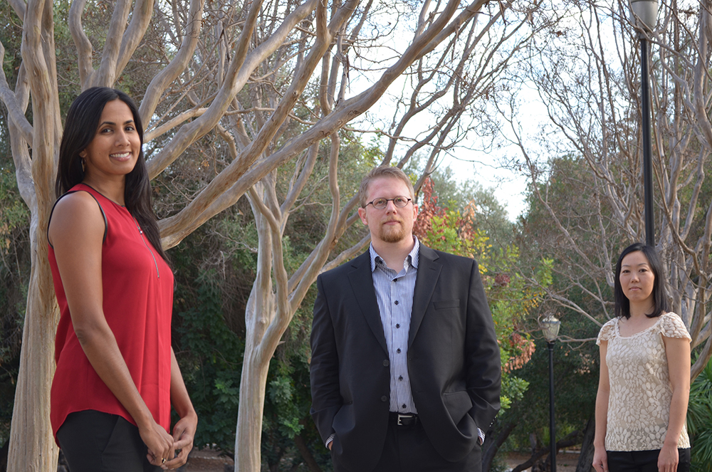 A half body group shot of, from left to right, Shalini Vijayan, Aron Kallay, and Yuri Inoo, standing in a park-like outdoor setting.