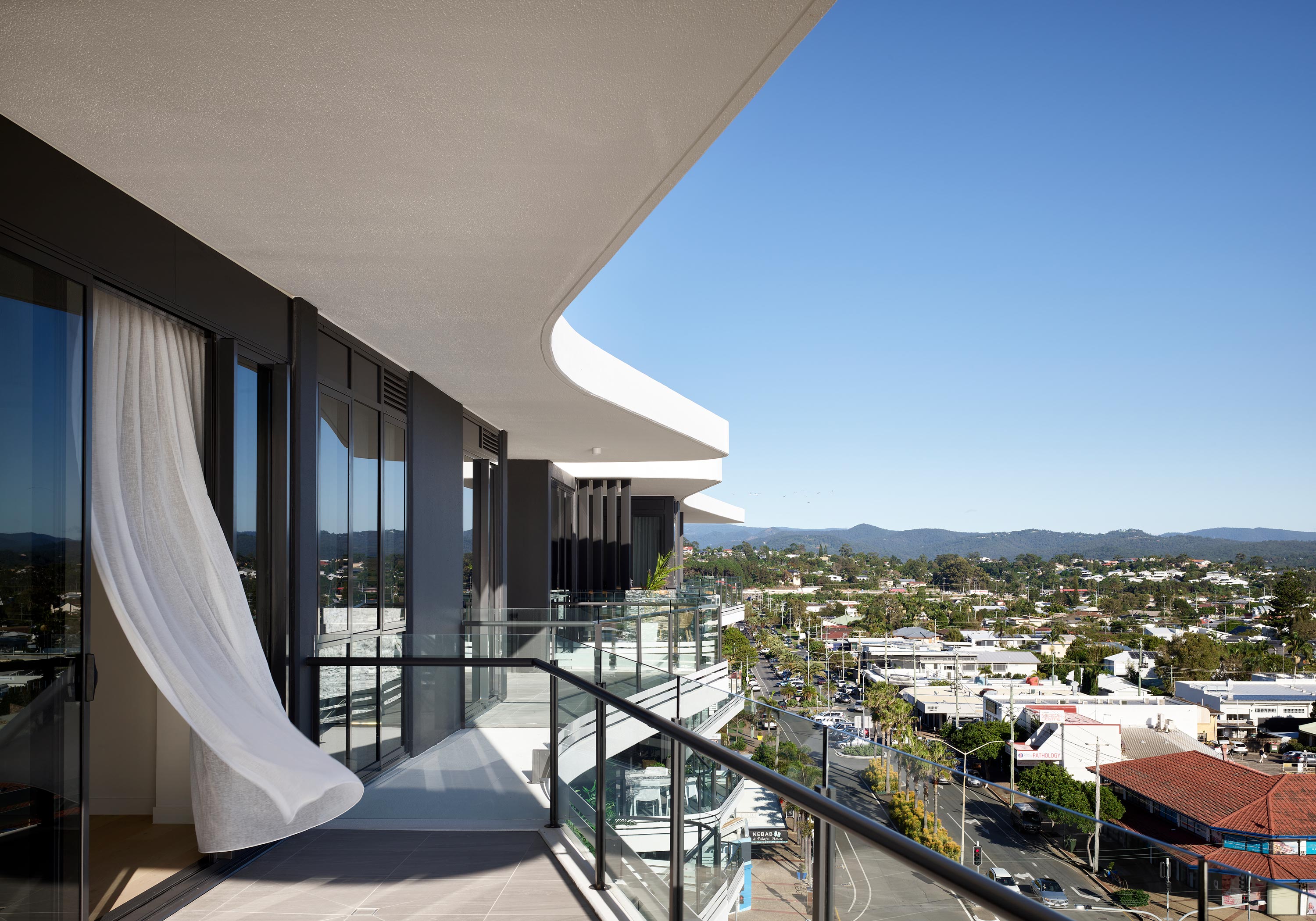 A spacious apartment balcony with a flowing white curtain overlooking neighbouring residences.