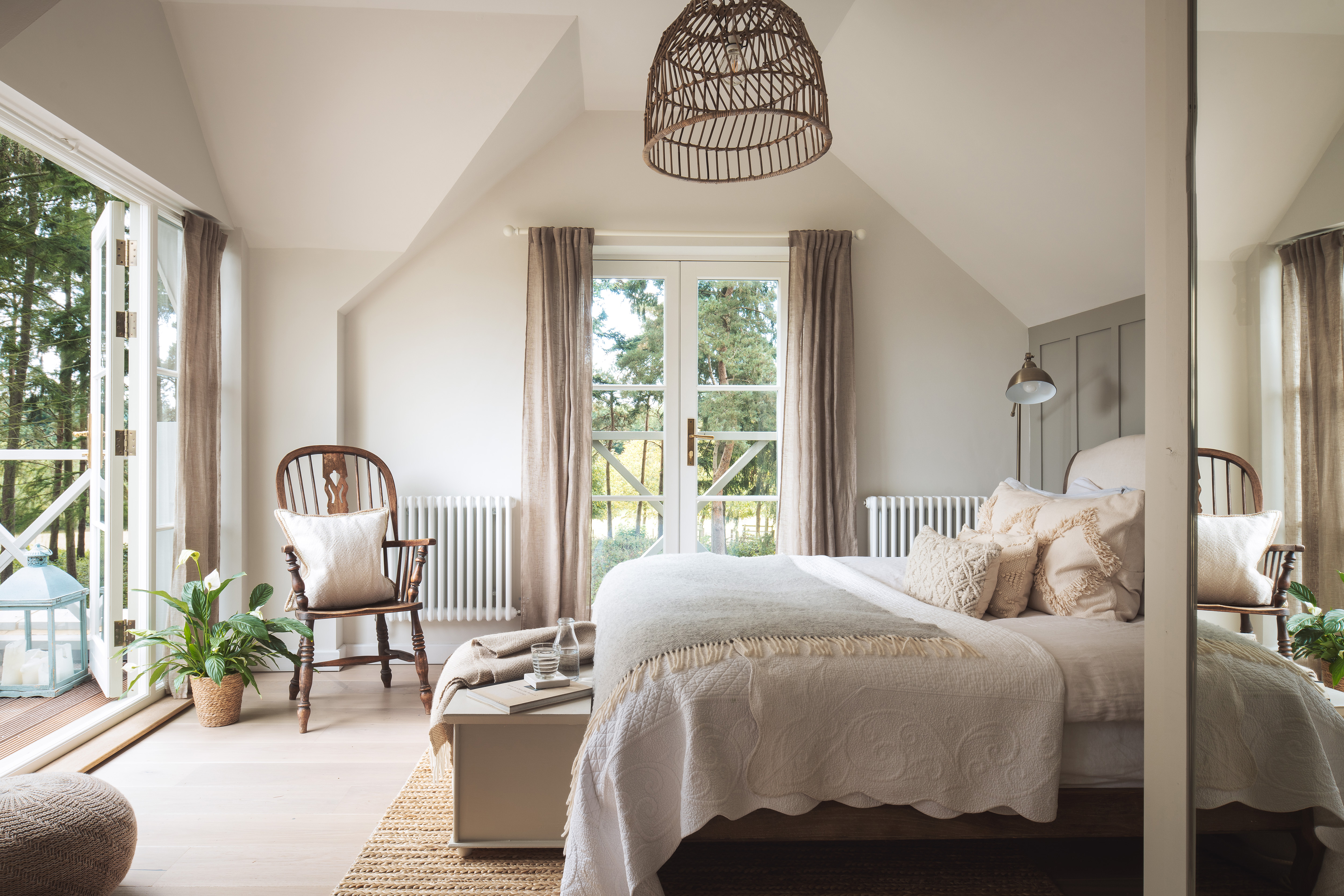 Cosy, neutral bedroom with double bed in neutral colour palette with wooden furnishings, house plant and woven lampshade.