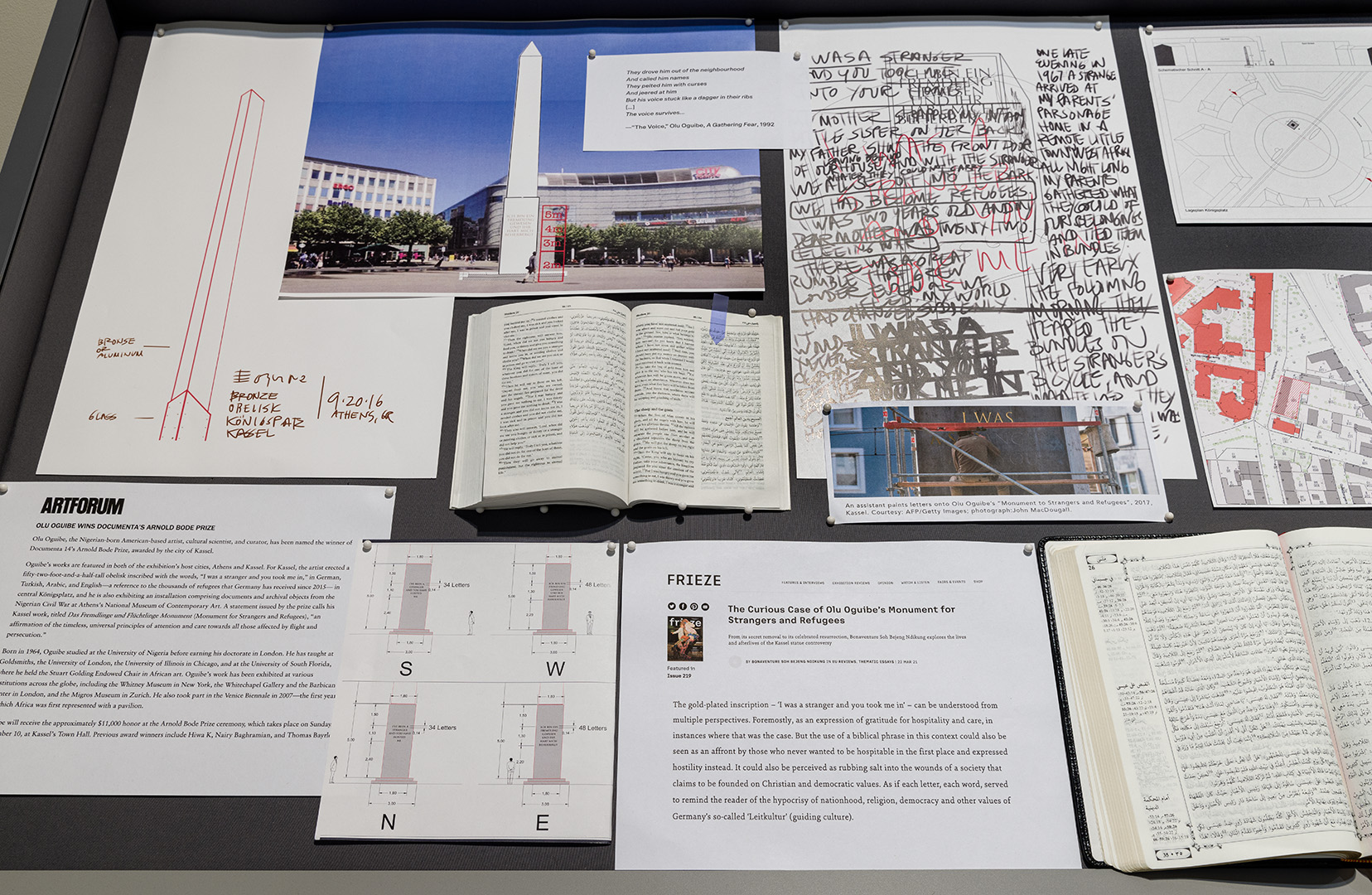 Olu Oguibe, "A Monument for Strangers and Refugees," 2017, documentation and ephemera related to Olu Oguibe&rsquo;s "A Monument for Strangers and Refugees," an obelisk created for documenta14 in Kassel, Germany. Materials include renderings, press coverage, images,  three Arabic language bibles, which Oguibe used to finalize the Arabic translation of Matthew 25:35, iPad with drone video of the obelisk from 2017. Photo by Etienne Frossard. 