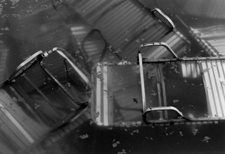A black and white image showing a disordered stack of pool chairs in a deserted pool at LeSourdsville Lake Amusement Park, in Monroe, Ohio.