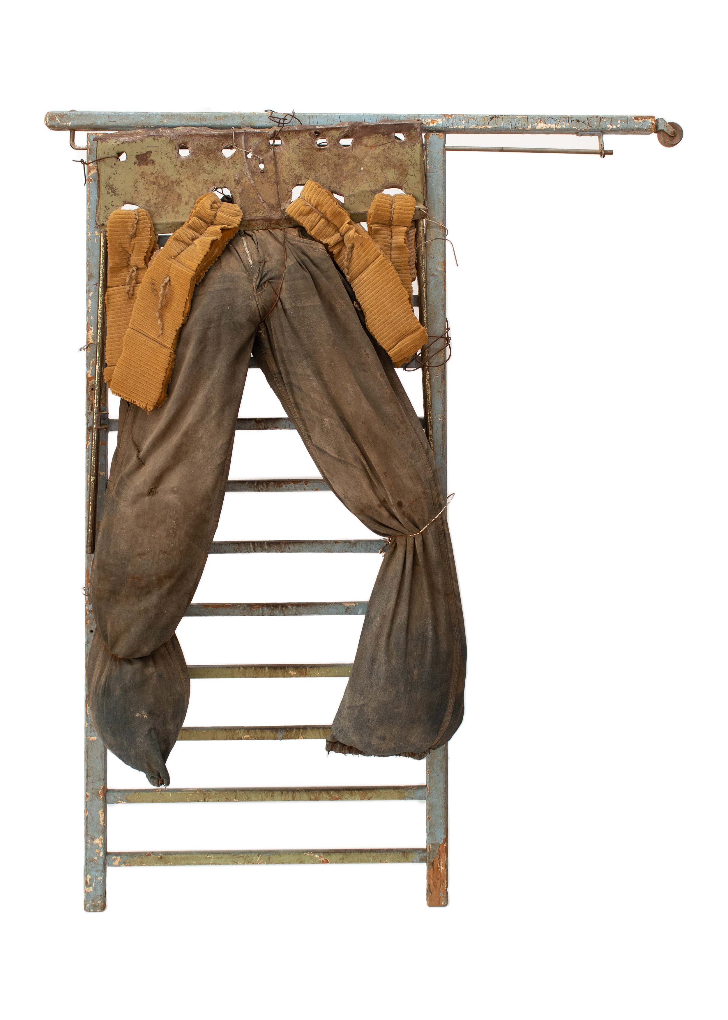 A abstract assemblage sculpture on a white background that consists of a pair of large, stuffed dark jeans that are fixed to a metal frame in a way that resembles window curtains.