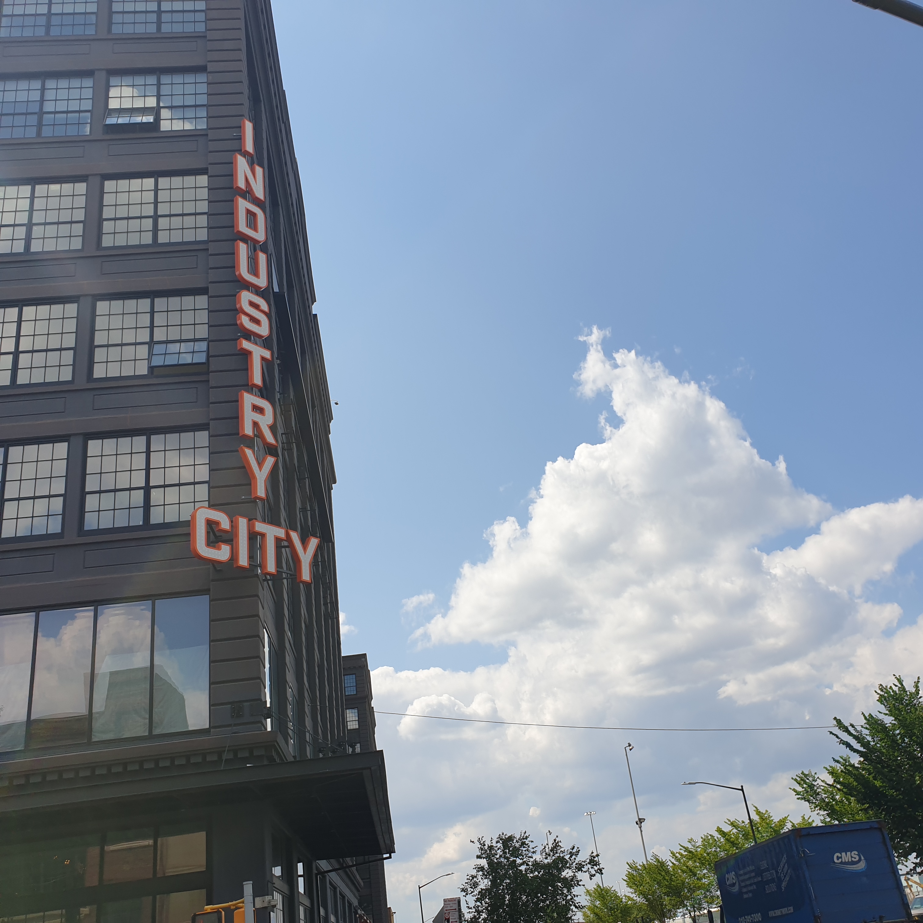 The side of a building with a sign reading Industry City. A bright white cloud can be seen against a blue sky.