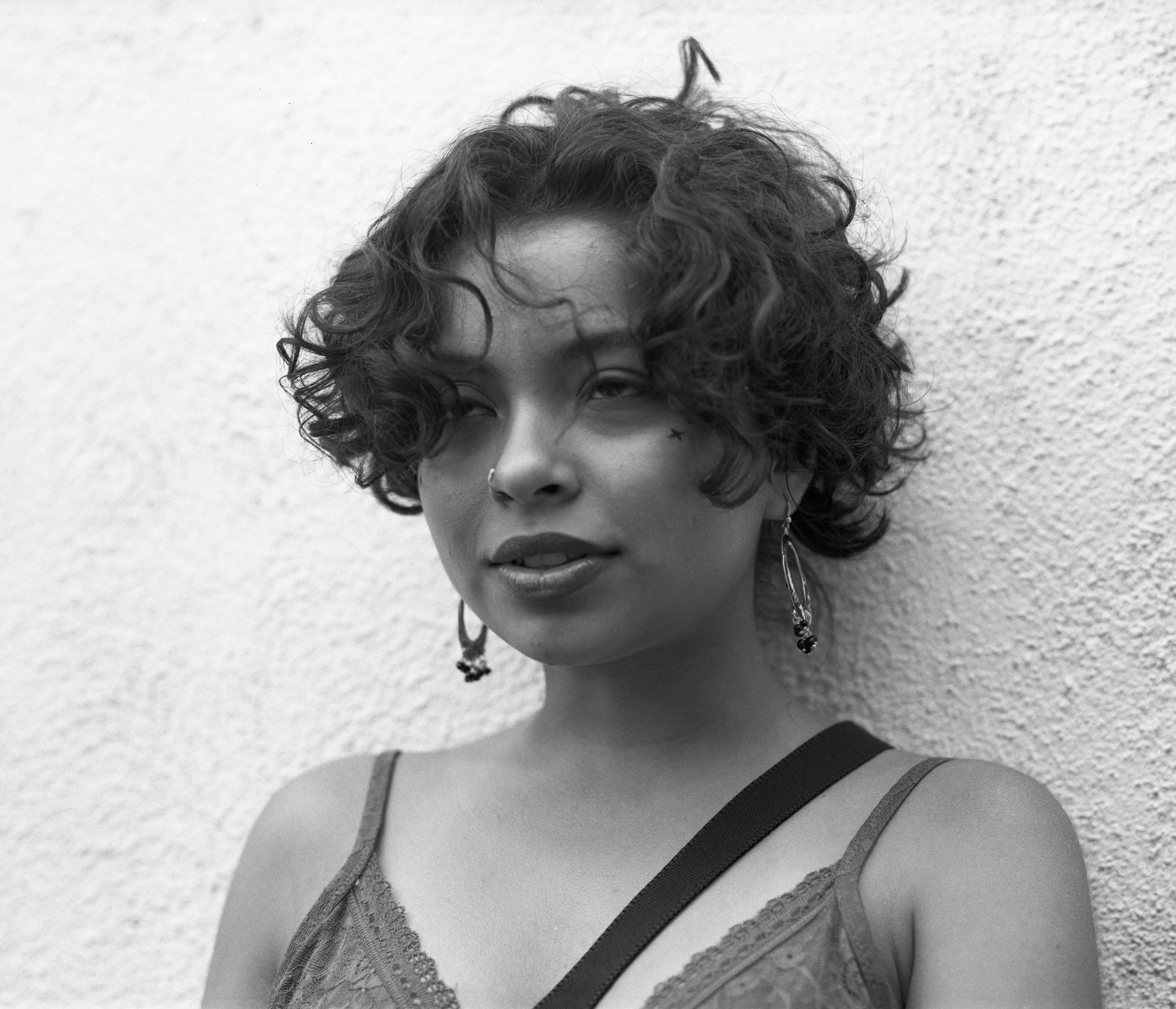 Black & White portrait of girl with curly hair. She wears hoop earring and is rolling her eyes