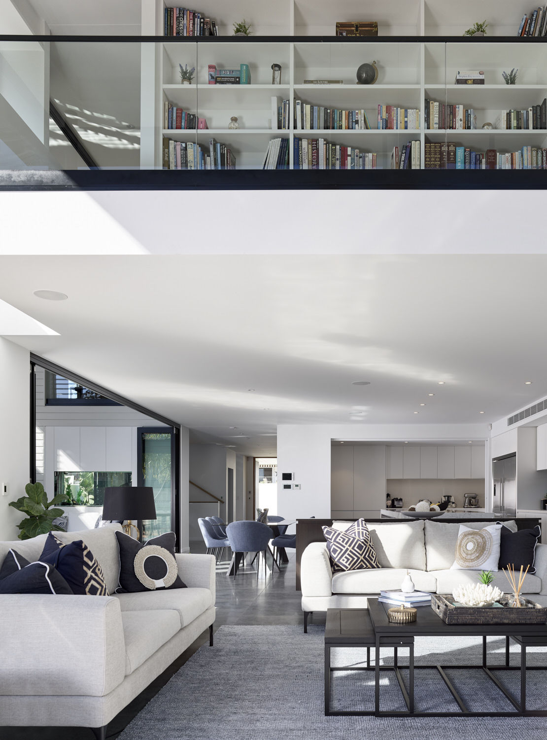 Two level interior view of a contemporary home, with generous living room on the ground level and library above.