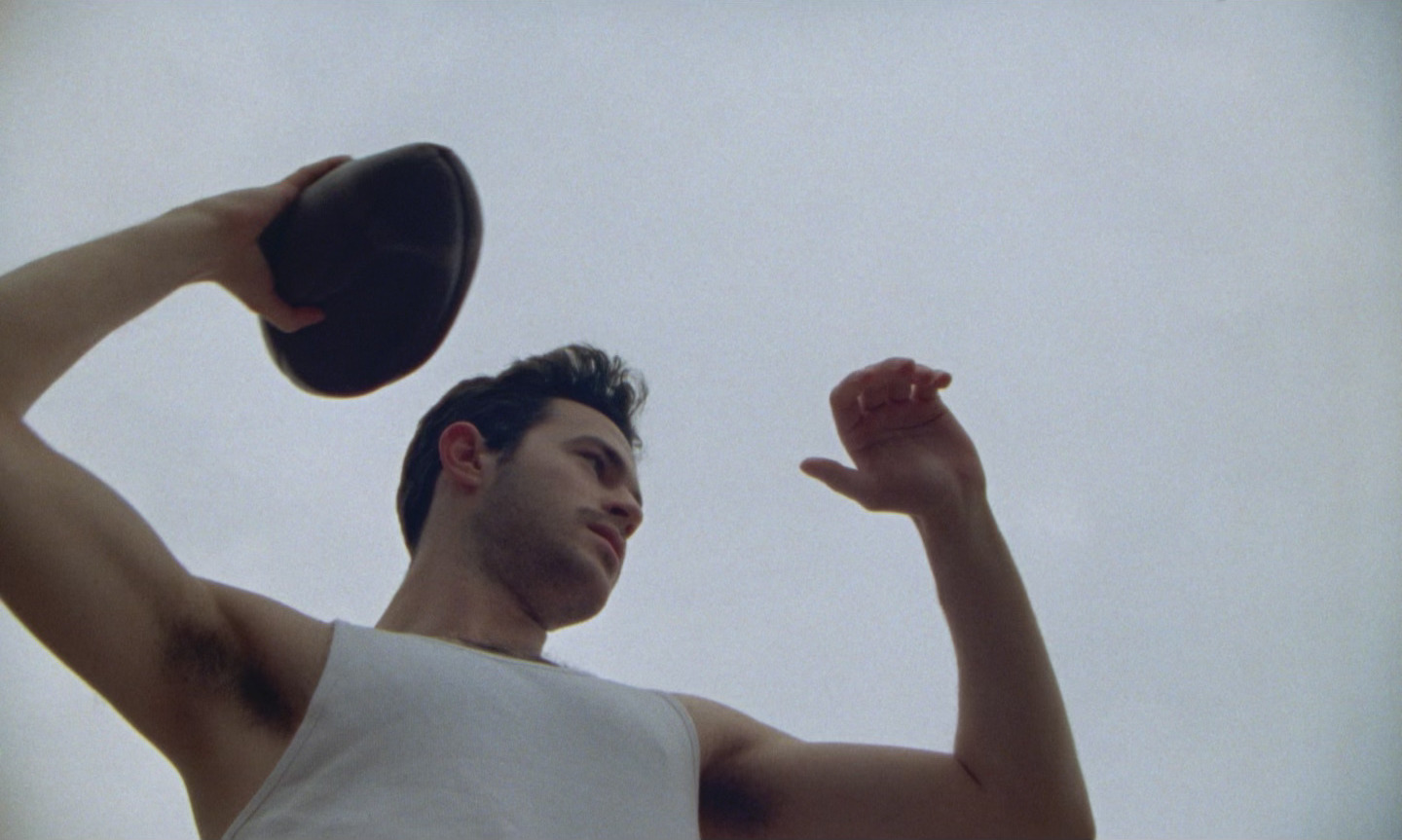still from film showing man in white tank top throwing a football