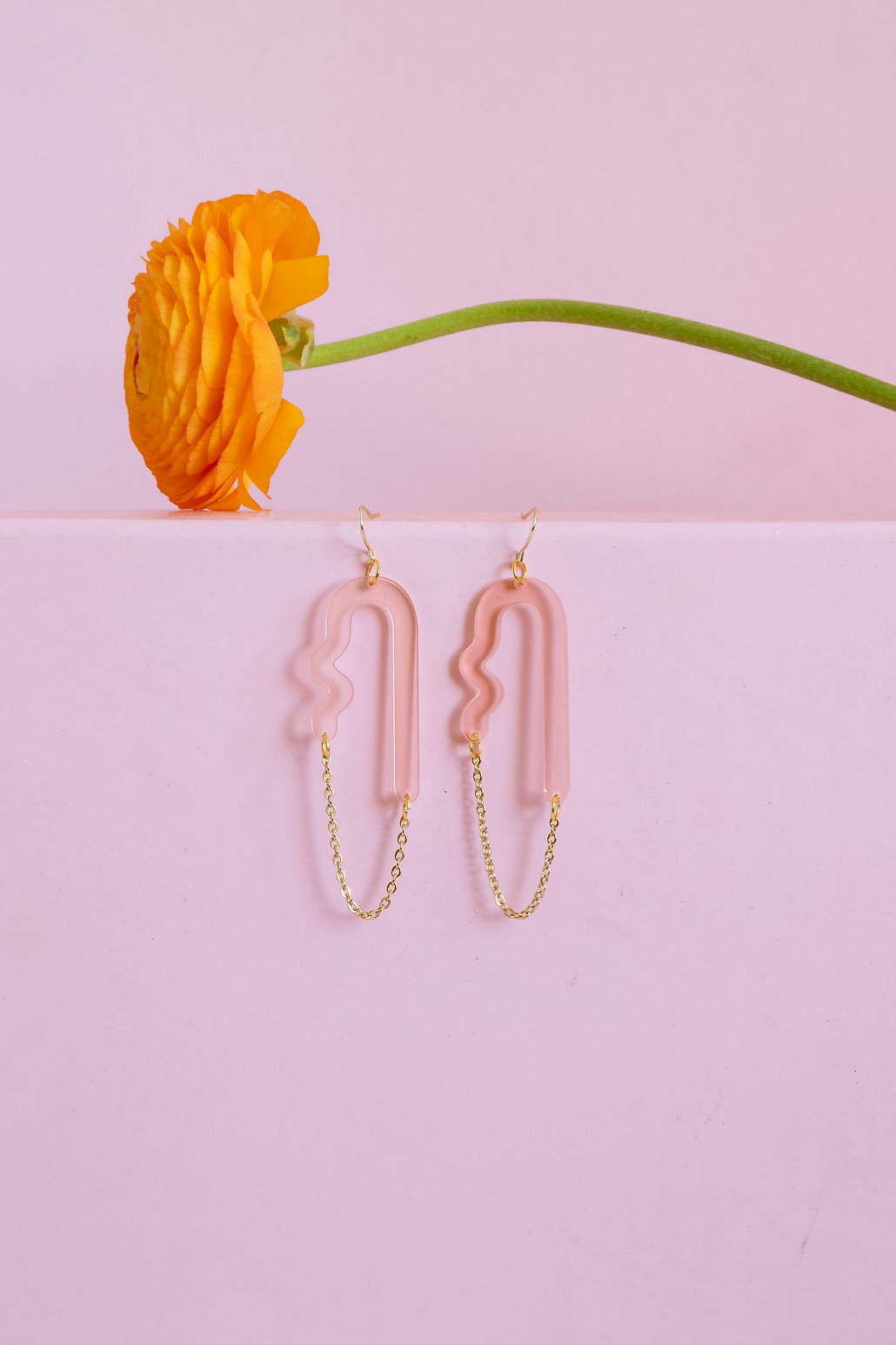 A pair of earrings by Sunny Side Studio, with an orange flower displayed above them