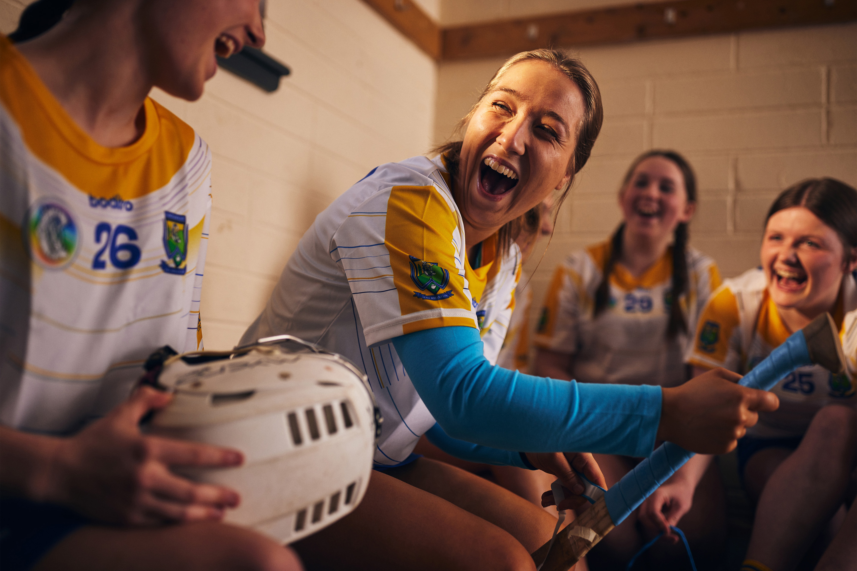 Camogie players laughing in a dressing room, photographed by Dublin-based lifestyle, fashion, and advertising photographer Alex Sheridan for Electric Ireland and Droga5 Dublin, capturing authentic energy and real moments