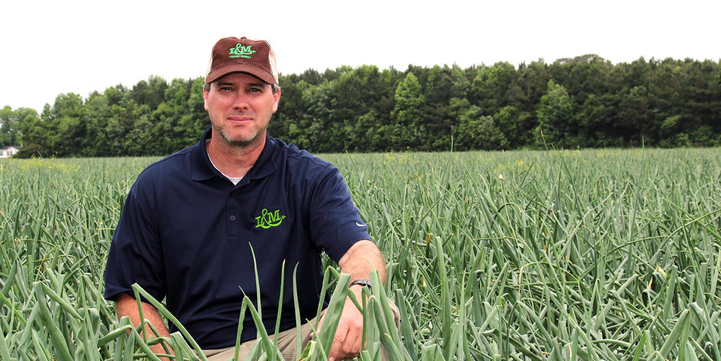 Farmer posed in a field, looking at the camera, with a brown L&M hat and navy L&M shirt