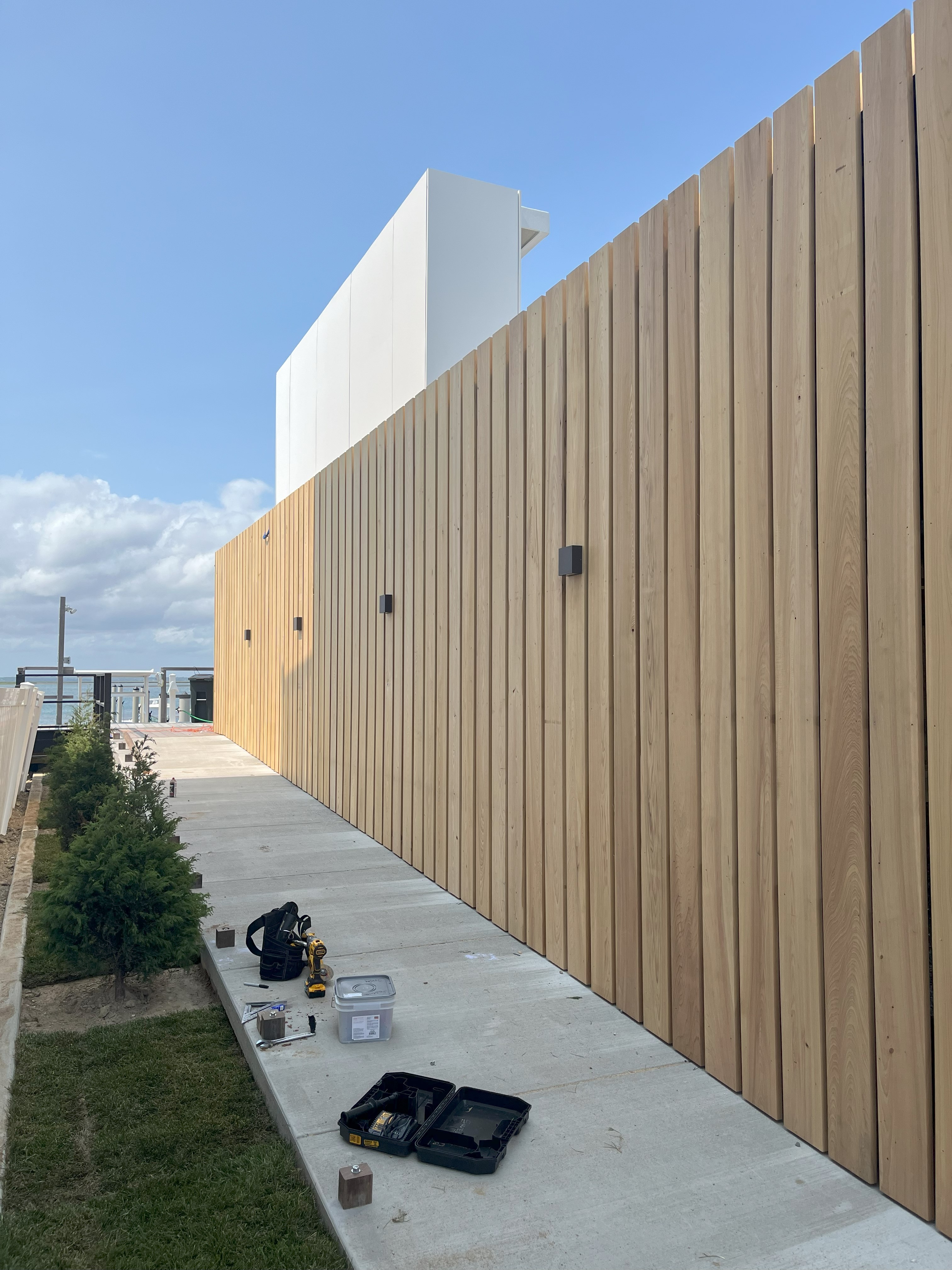Exterior construction photo of the Brigantine Marina Paddle Club, highlighting the modern vertical wood-slat fencing along a finished concrete walkway.