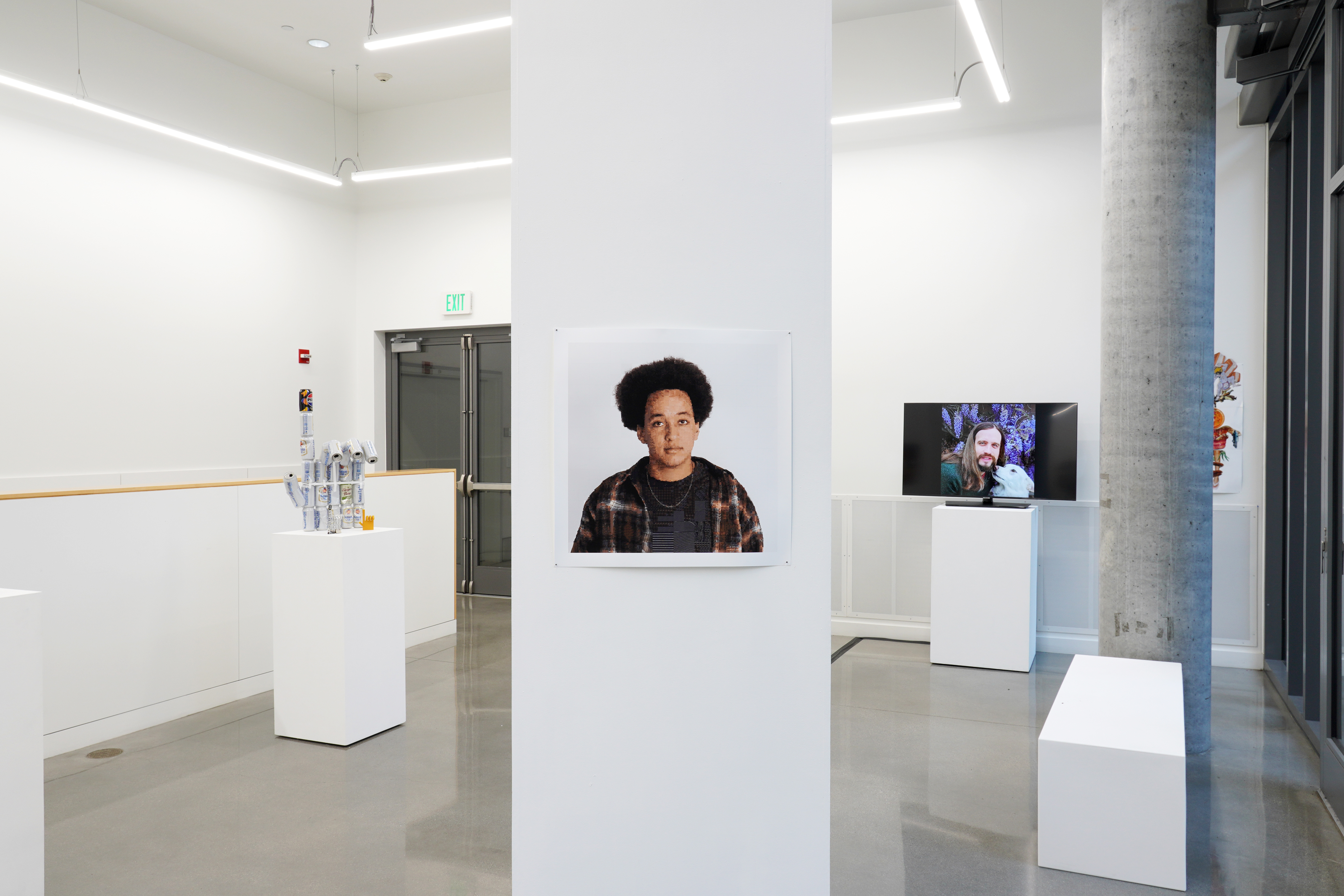 Two two-dimensional works in photography and collage hanging on the wall, a video artwork displayed on a monitor, and a few sculptures made of cans and other recycled materials placed on a pedestal.