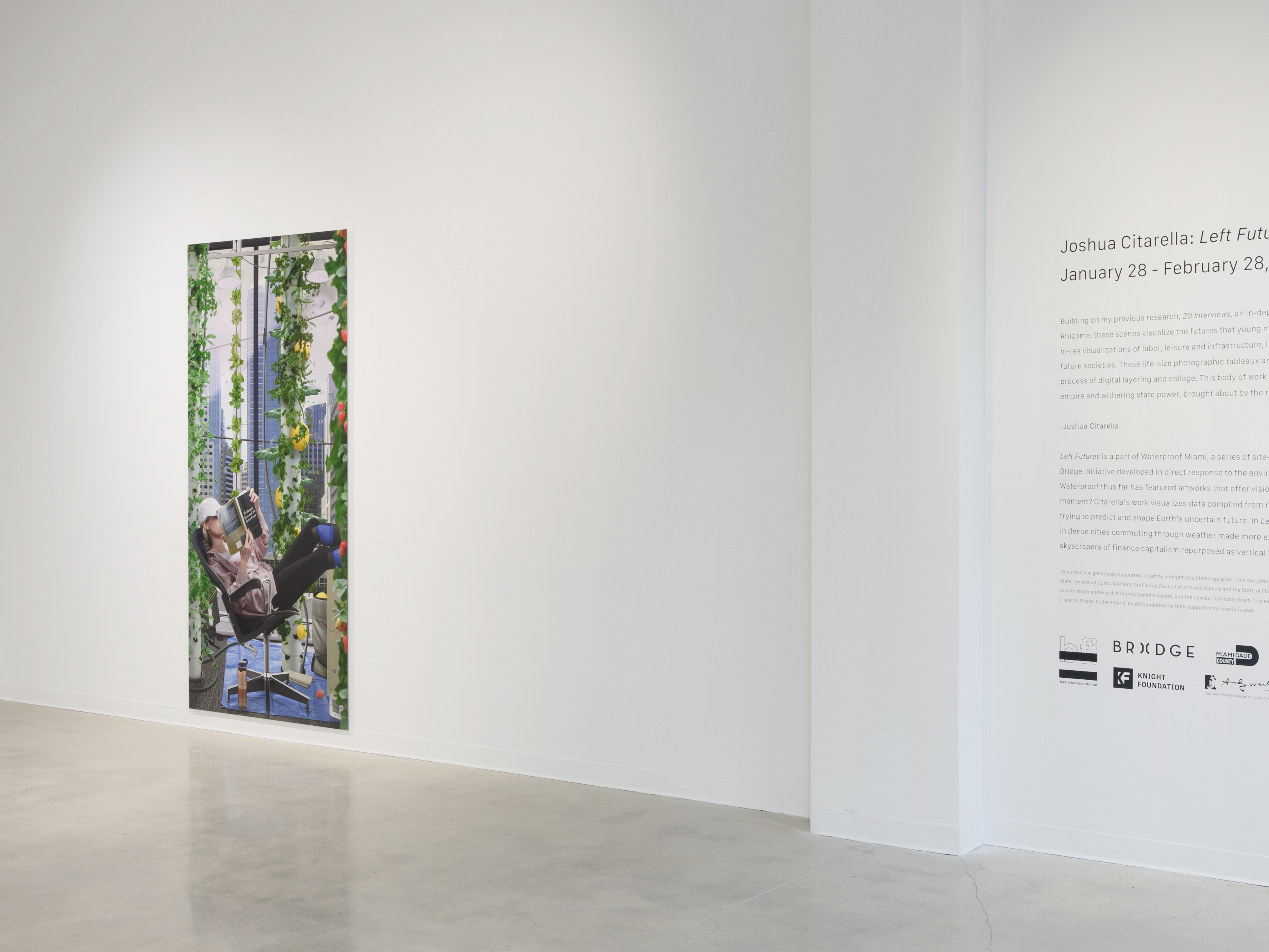 Installation view of “Left Futures” by Josh Citarella. 2021. Presented by Bas Fisher Invitational and Bridge Initiative. Citarella’s Use-Value Urban Repurposing is displayed on a white wall to the left, as a silver wall text displaying the artist and the exhibition’s purpose is printed on the white wall on the right.