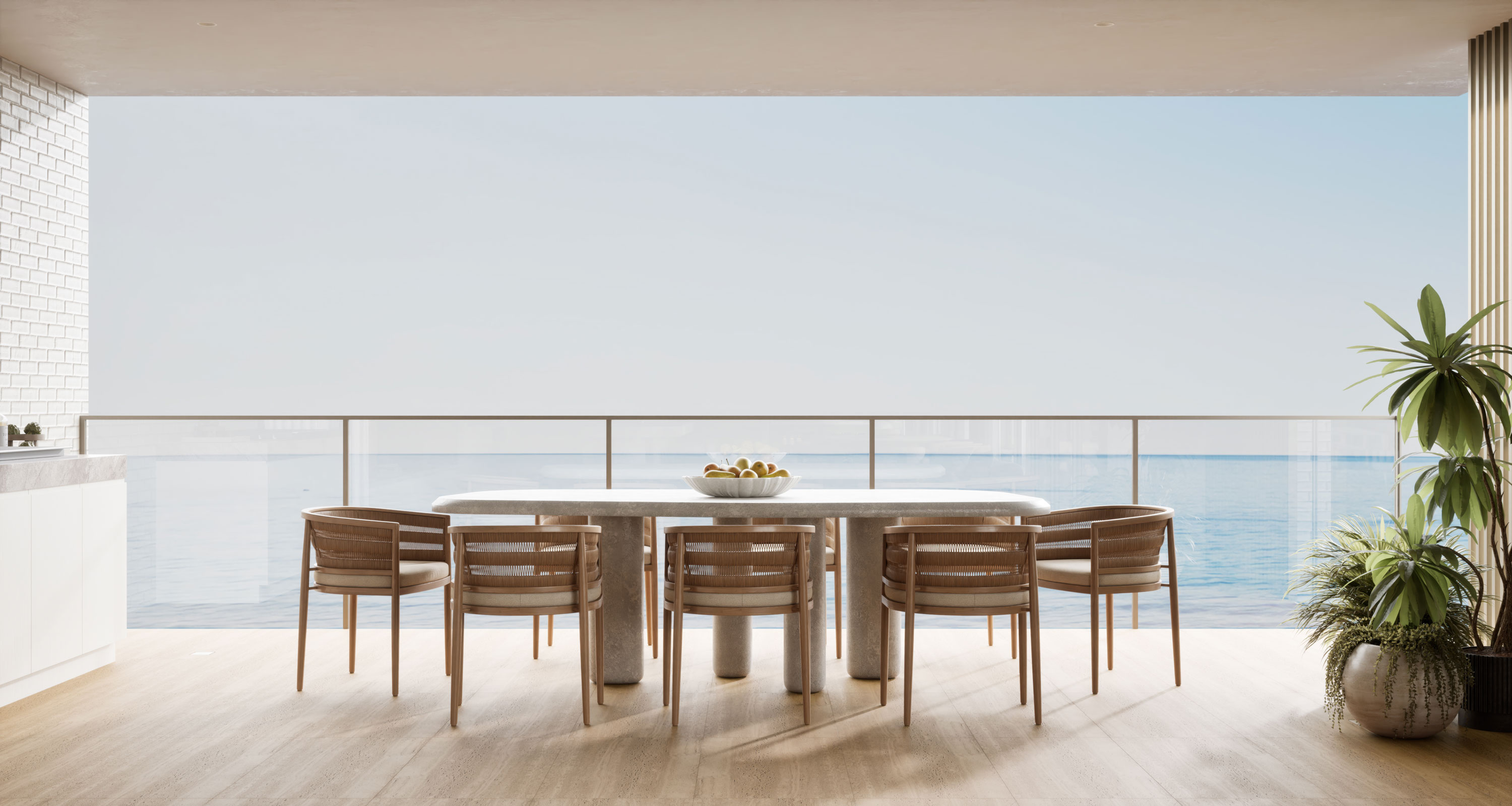 Elegant oceanfront dining terrace featuring a sleek white stone table set with woven armchairs for six, a central bowl of fresh fruit, warm wooden flooring, and potted tropical plants, all framing breathtaking views of the sparkling blue sea under a serene sky.