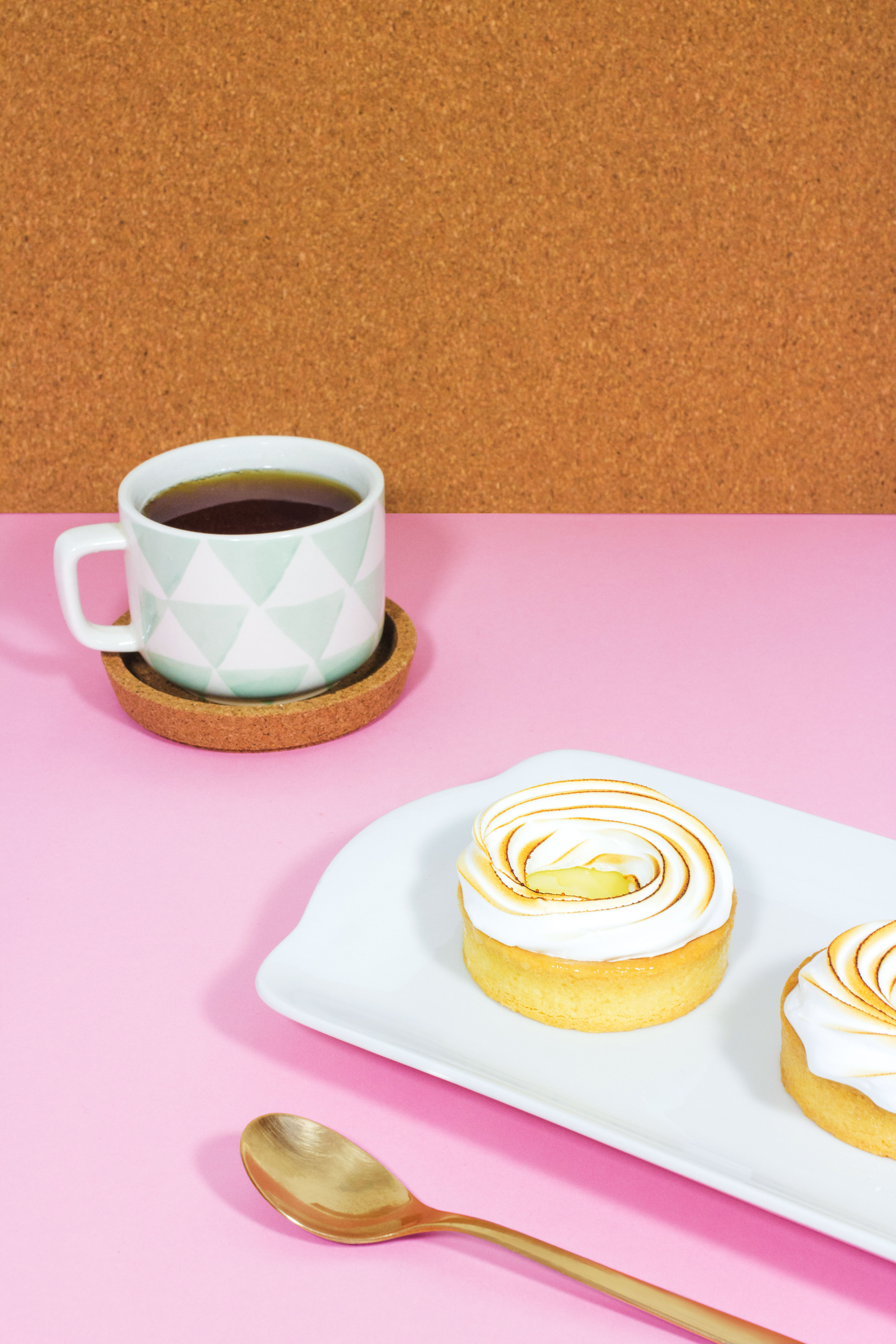 A minimalist representation of a "Fika" using sweet pastry and coffee, in a pink set with cork wall.