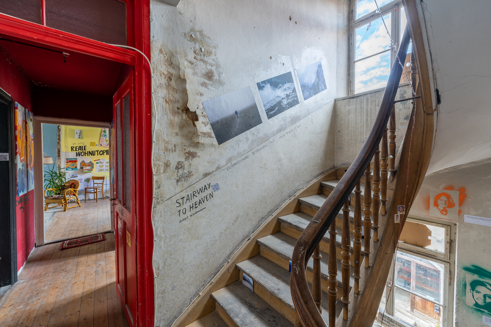 Bild 1 zu Stairway to heaven: Holztreppe mit Treppengel&auml;nder, die in den Dachboden f&uuml;hrt. An der Wand links der Treppe, sowie unter den Treppenstufen, befinden sich Fotografien von Robert Wiedemanns Bergbesteigungen.