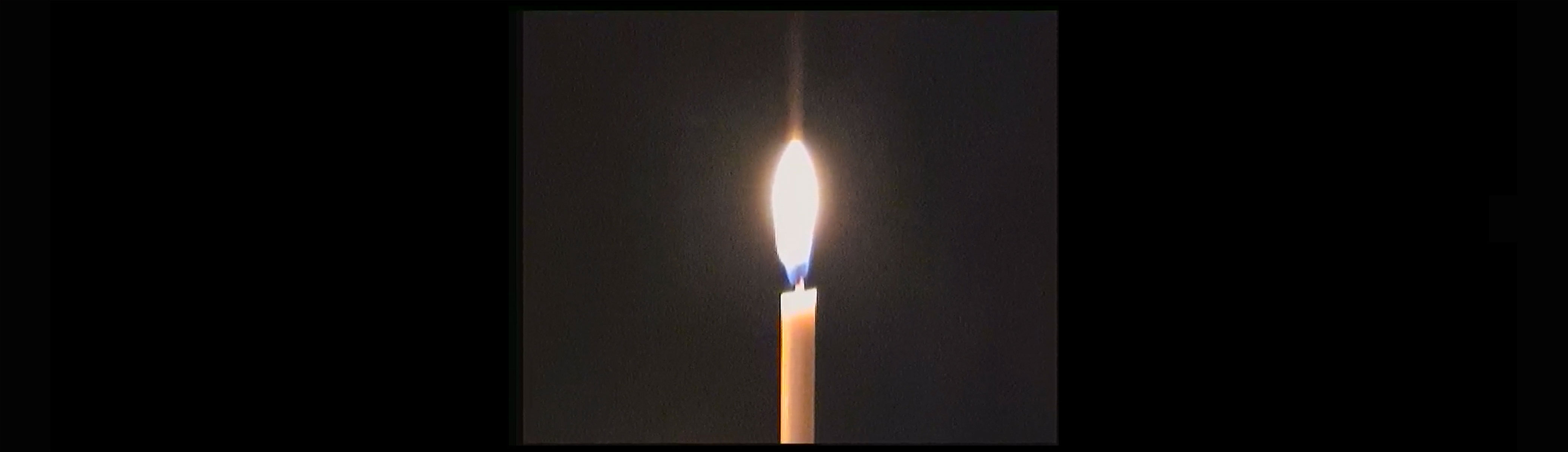 1/1 — CANDLE AND HEARTBEAT.This work combines a video recording captured on Hi8 footage in St. Stephens Cathedral in Vienna, Austria, along with a sound recording made by the artist of her heartbeat at home in Chicago. Both media elements, executed in single takes, possess a slight unsteadiness, reminding us of her body's presence. The imagery of a solitary burning candle references a common religious practice of remembering those who have passed. As the minimal and soft flame flickers with the low decibel of her heartbeat pulses, Quinn intends to evoke contemplation of our bodies, the present, and our mortality.Video still (Full video 00:01:58), shot on Hi8 and digitized, 2022.