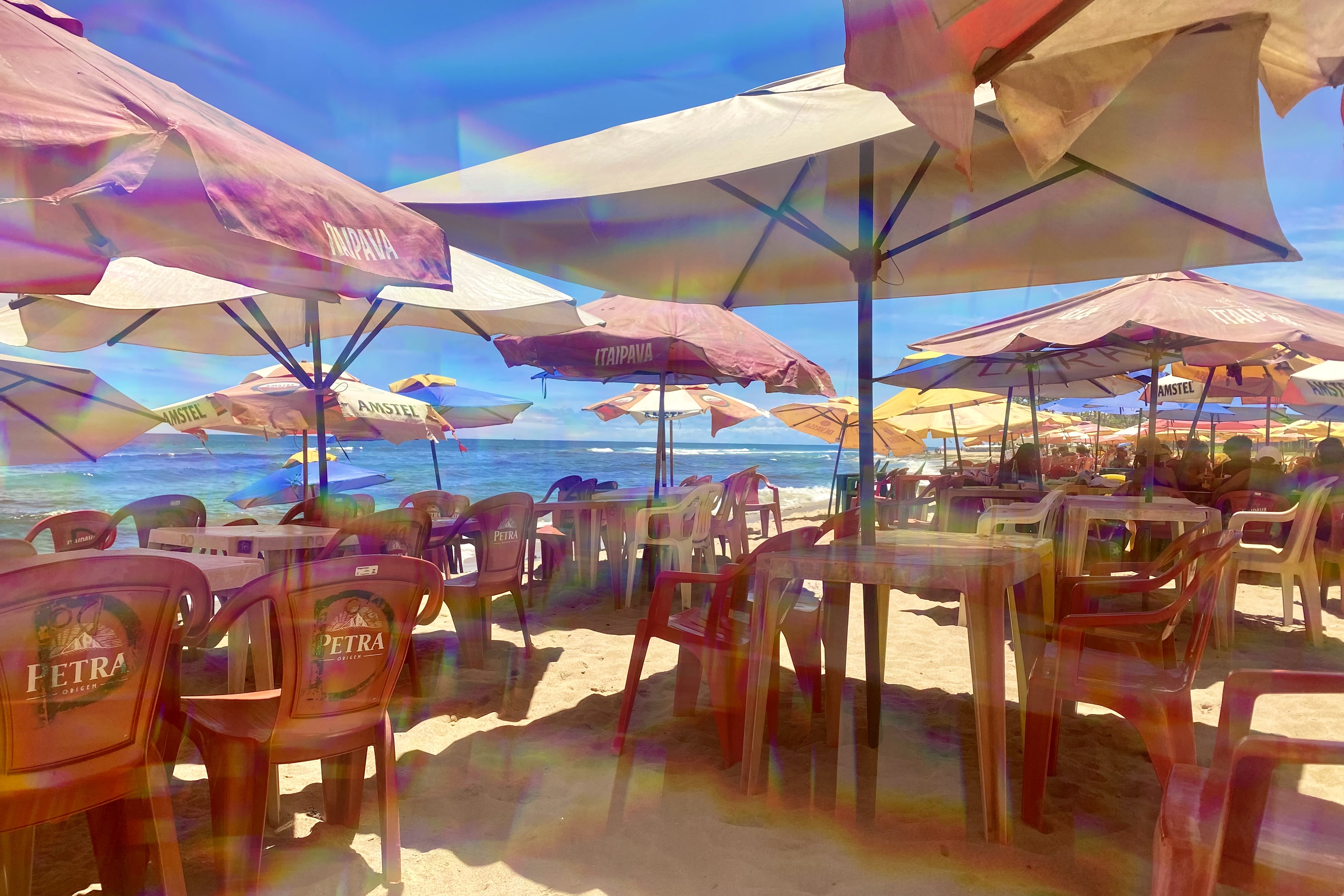 A beach in Salvador, Bahia, Brazil, featuring tables and chairs under colorful umbrellas.