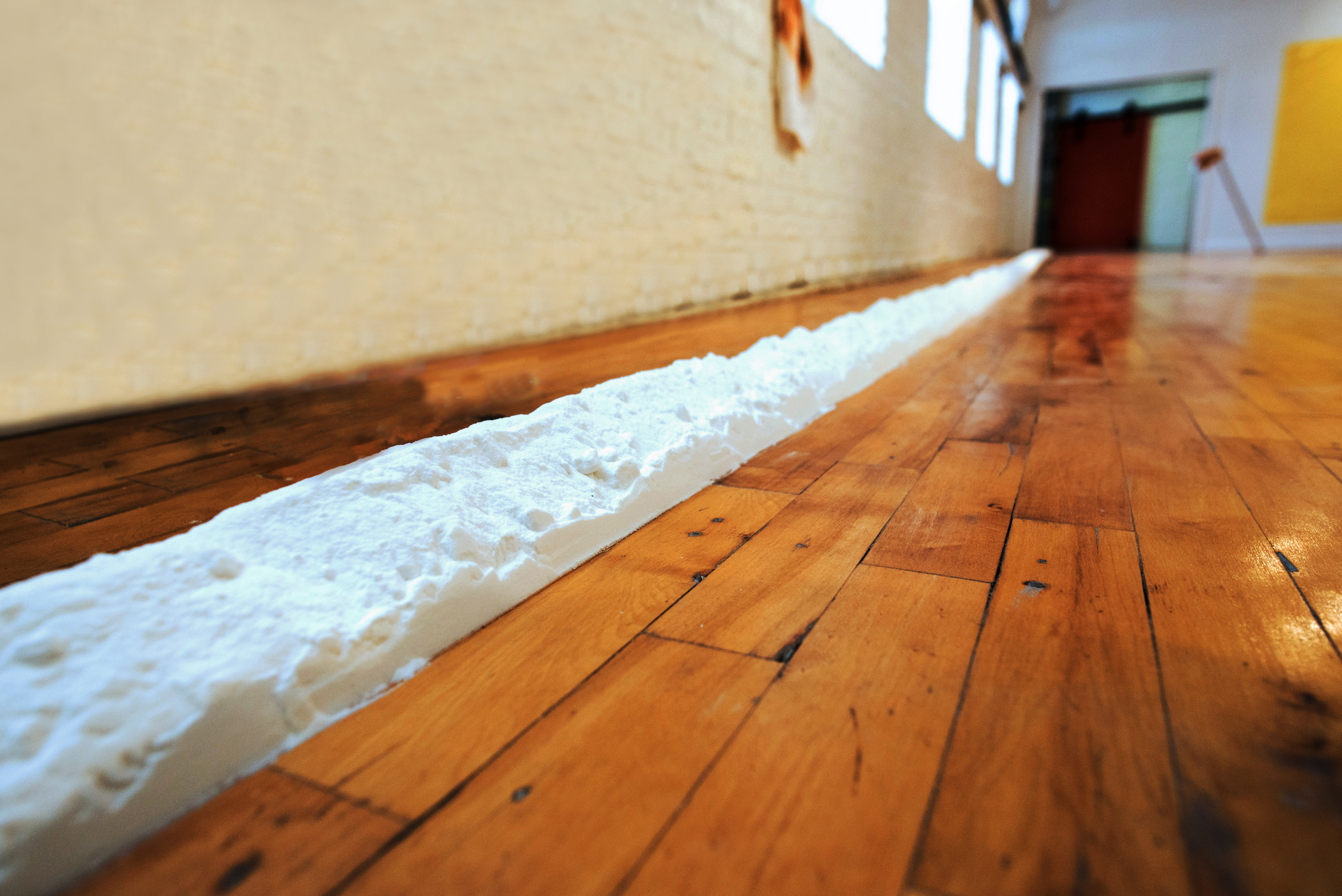 3/3 — A WALL OF FLOUR.  The site-responsive installation A Wall of Flour. 6.12.15 was created for the exhibition Body Mass Index, curated by George William Price.  150 lbs. sodium bicarbonate, floor, dimensions variable, approximately 6" x 540", the distance between work and wall/windows equal to reach of the artist's/activator's arms, 2015.