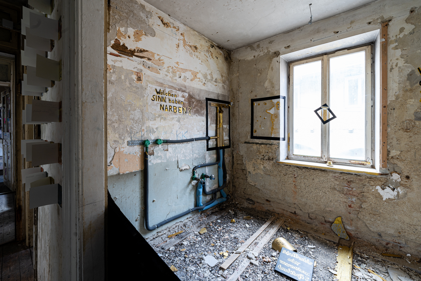 Bild 2 zu Sch&ouml;nheit der Narben: Blick auf die linke Wand im Raum. Der Raum ist nicht begehbar, er ist nur vom Gang aus betrachtbar. An der Wand steht mit Druckbuchstaben: Welchen Sinn haben Narben?