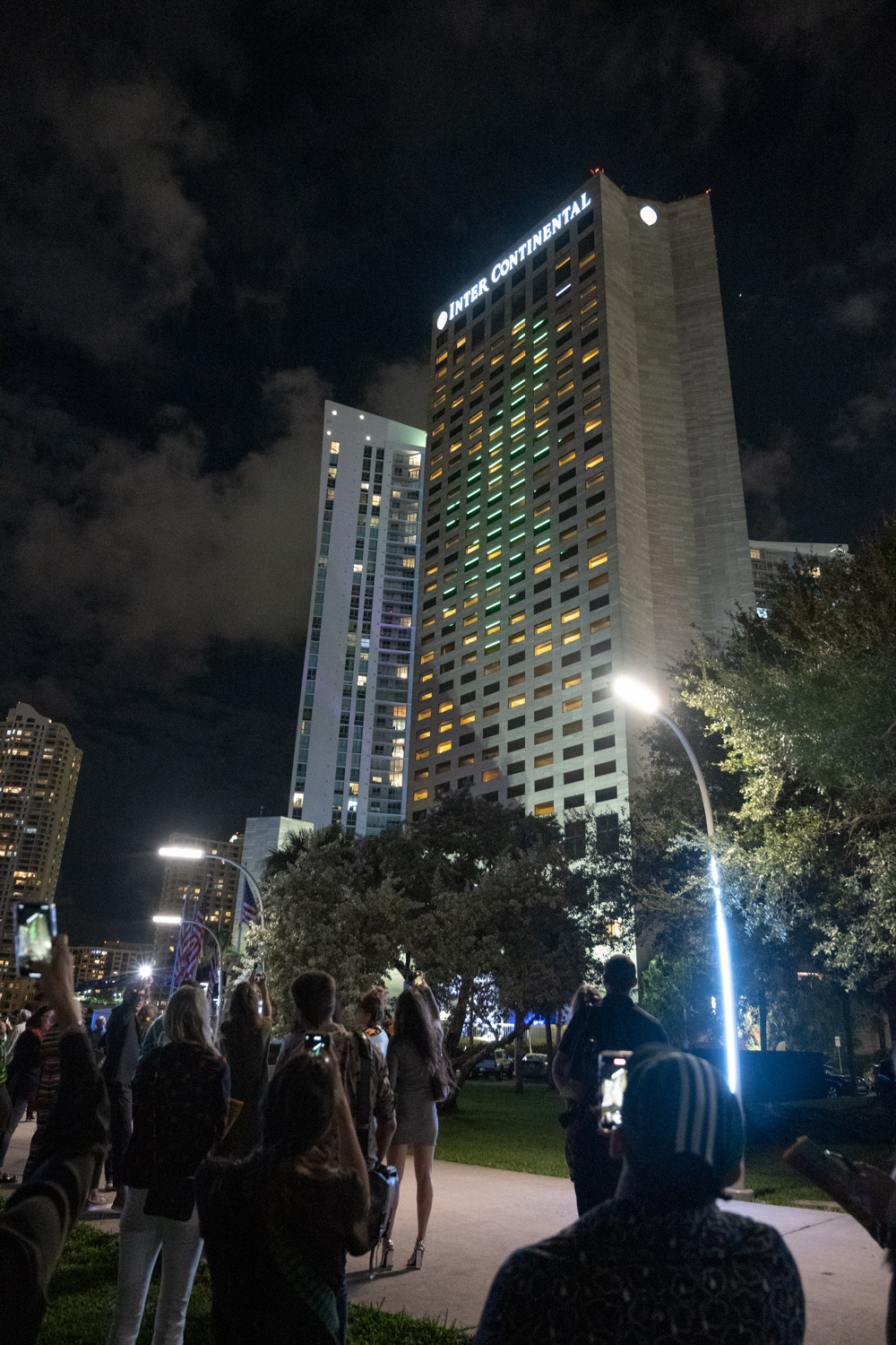 As wildlife crawls across the facade of the InterContinental hotel, people in the foreground are documenting the installation on their phones.