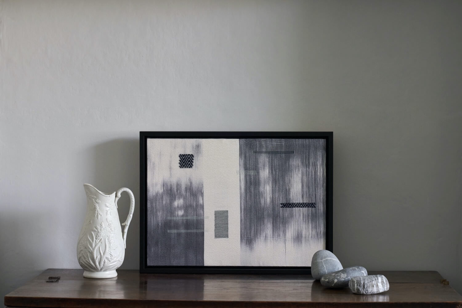 A framed textile in indigo and white leaning against a wall on top of a table