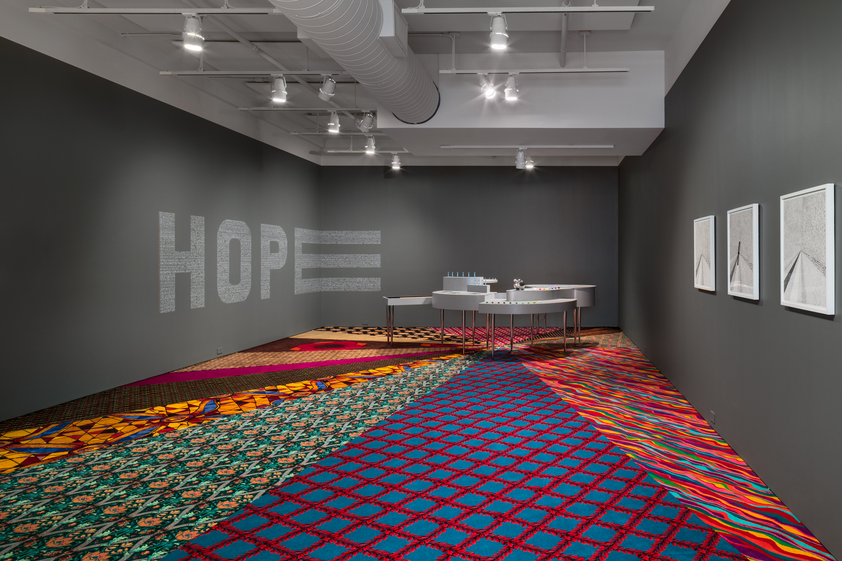 Installation shot, Statistics of Hope by Ghost of a Dream and Jennifer Dalton. From left to right: Statistics of HOPE, 2018. Paint pen on wall, 50 x 198 x 49 inches. Statistics of Chance, 2018. Mixed media, 40 x 125 x 160 inches. End Game, 2018. Triptych: ink on corkboard and paper, with spinner, dart, plexiglass and wood, each 25 x 23 inches. Where You Stand, 2018. Salvaged casino carpet, 21 x 36 feet. (Credit: Rafael Gamo)