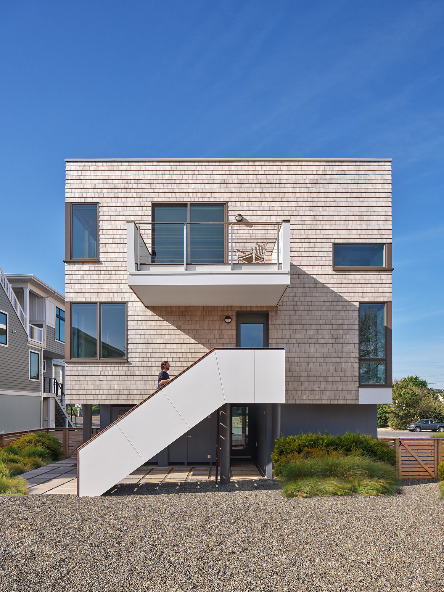 Exterior view of the Gap House North Elevation, highlighting the prominent white entry staircase, cedar shingle cladding, varied window sizes, and upper-level balcony.