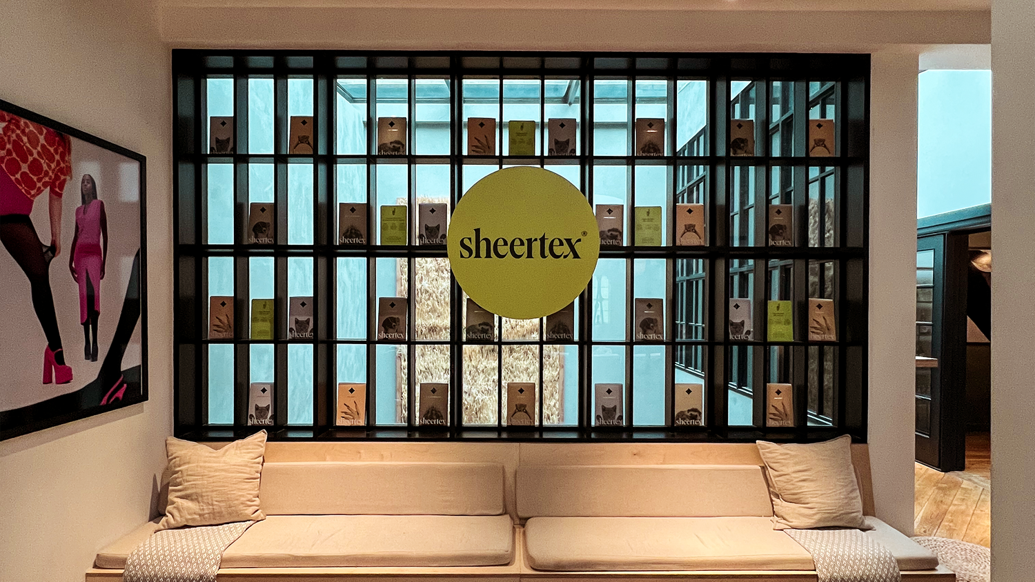 Sheertex pop-up interior with seating area and brand logo displayed on a black grid wall filled with product boxes.