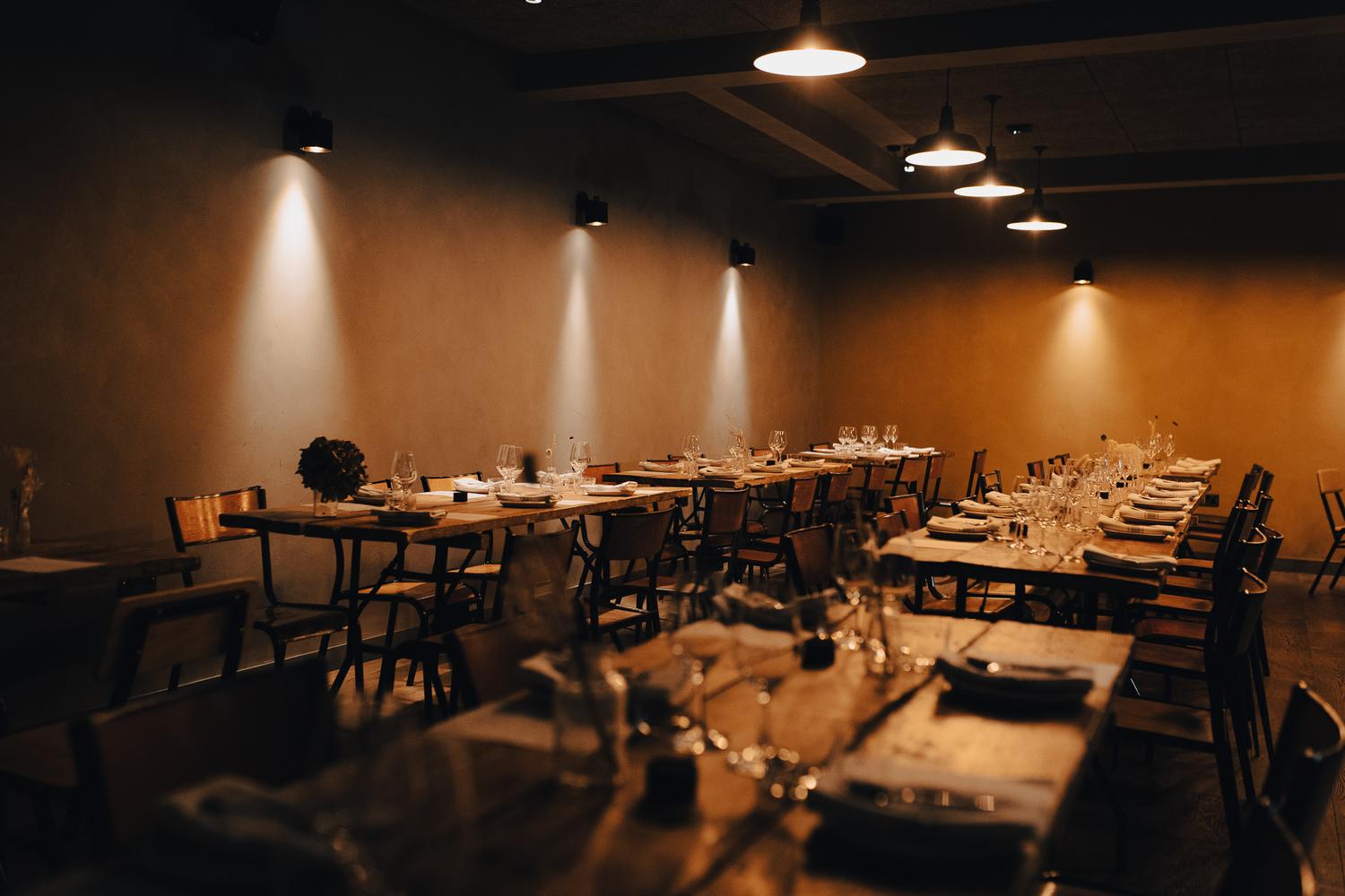 Long wooden tables set for Paired at Carousel London, with soft golden lighting and neatly arranged glassware and napkins.