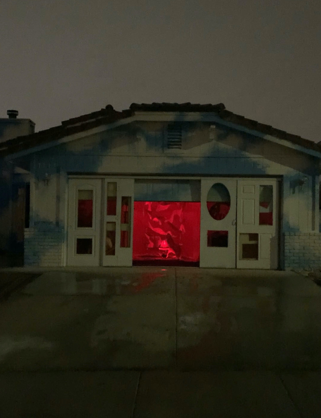 A wide shot from outside the exhibit space during the night time, where behind the walls is a room full of red and you see some floating pieces of paper floating in space