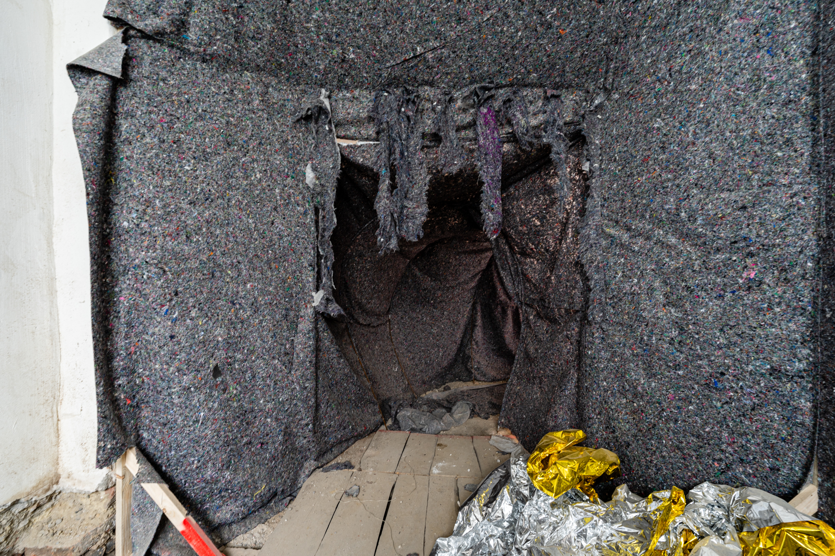 Bild 5 Stabsauber: Blick auf den Ausgang des Staubsaugerinneren in Richtung Tunnel. Am Boden liegt zusammengekn&uuml;llte Silberfolie. Graue Teppichfransen h&auml;ngen an der &Ouml;ffnung zum Tunnel herunter.