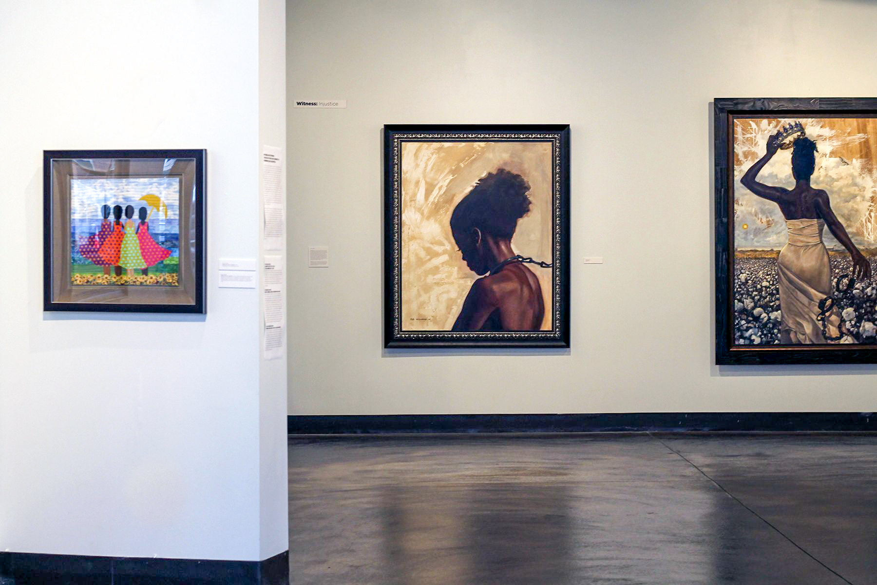 A gallery with two paintings in the distance, with a wall sticking out closer to the viewer with an additional painting on the left.