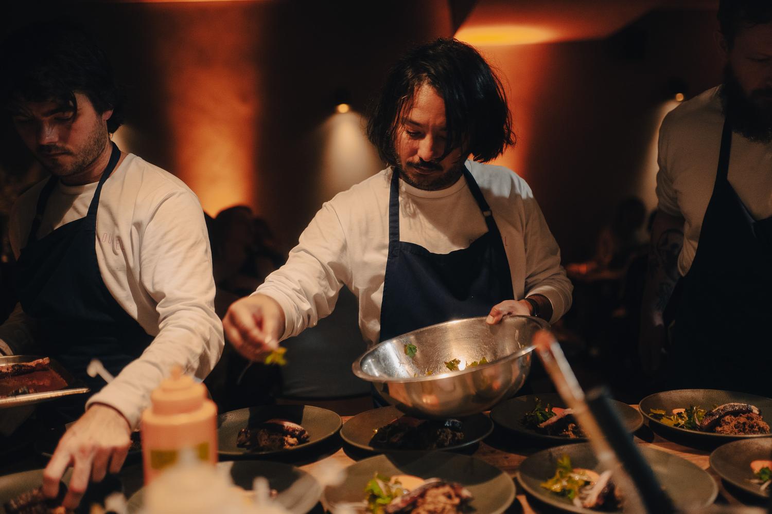 Chef Yuji Tani plating dishes in a warmly lit dining room during the Paired × Tate Modern event.