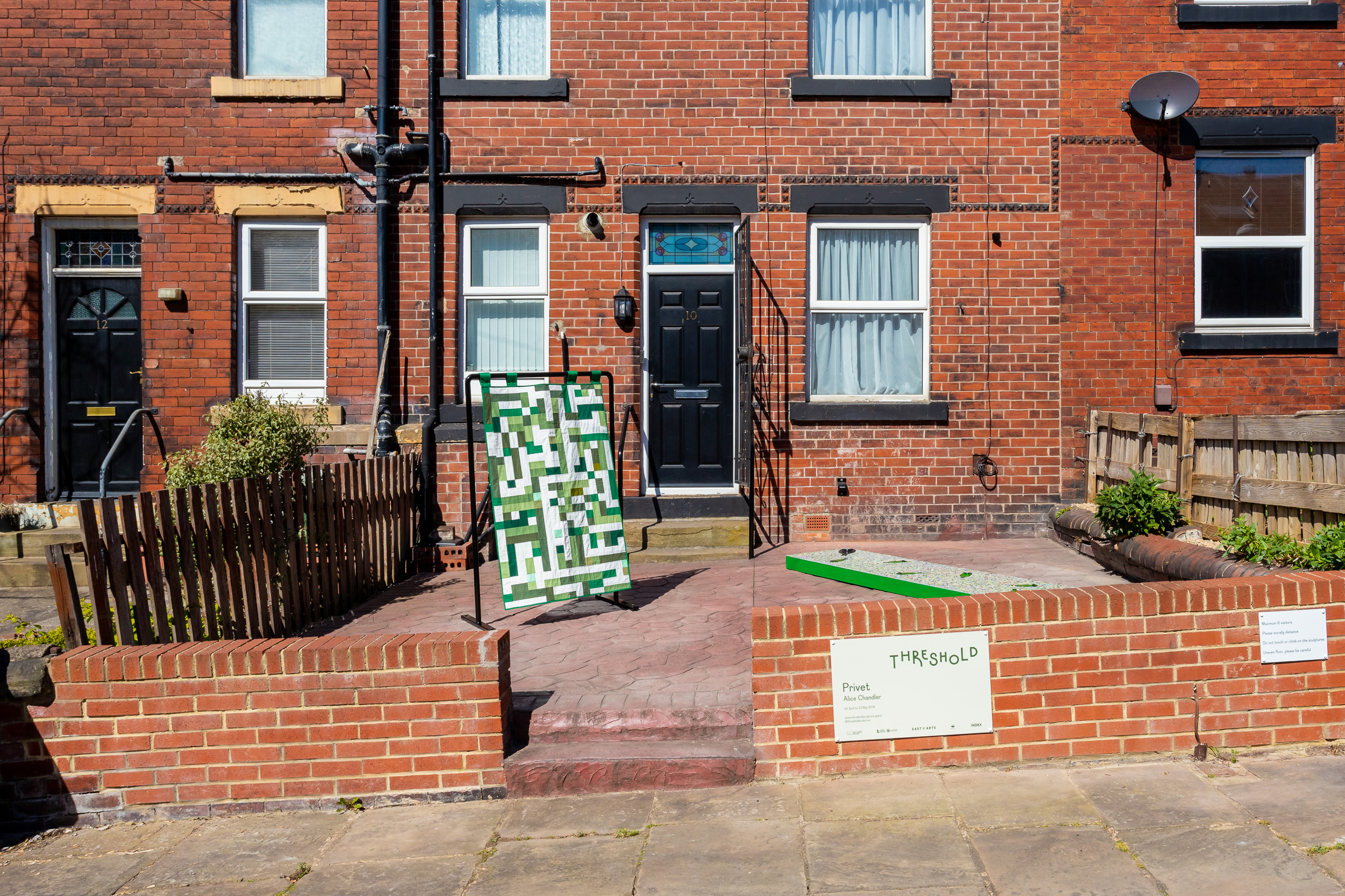View of Privet from the street. Two sculpture sit in a front yard in front of a terraced house.