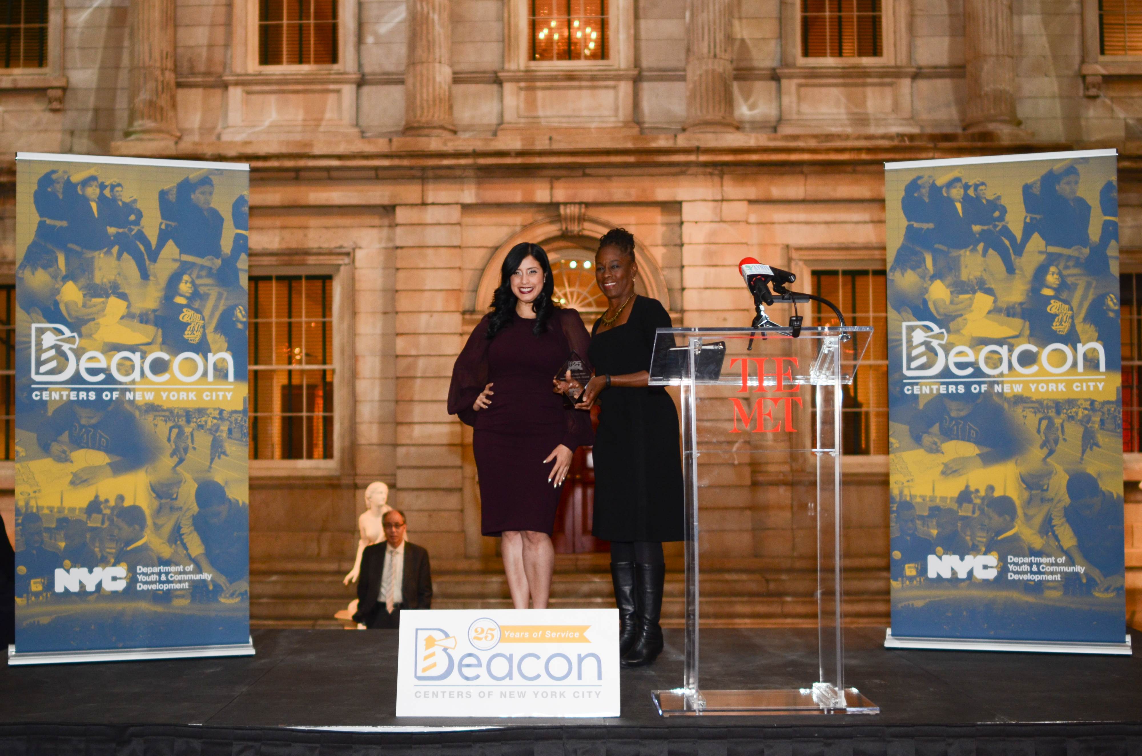 NYC First lady Chirlane McCray receiving an award on stage at the Met Museum. Two tall Beacon Center branded pop banners are displayed on both sides of the stage.